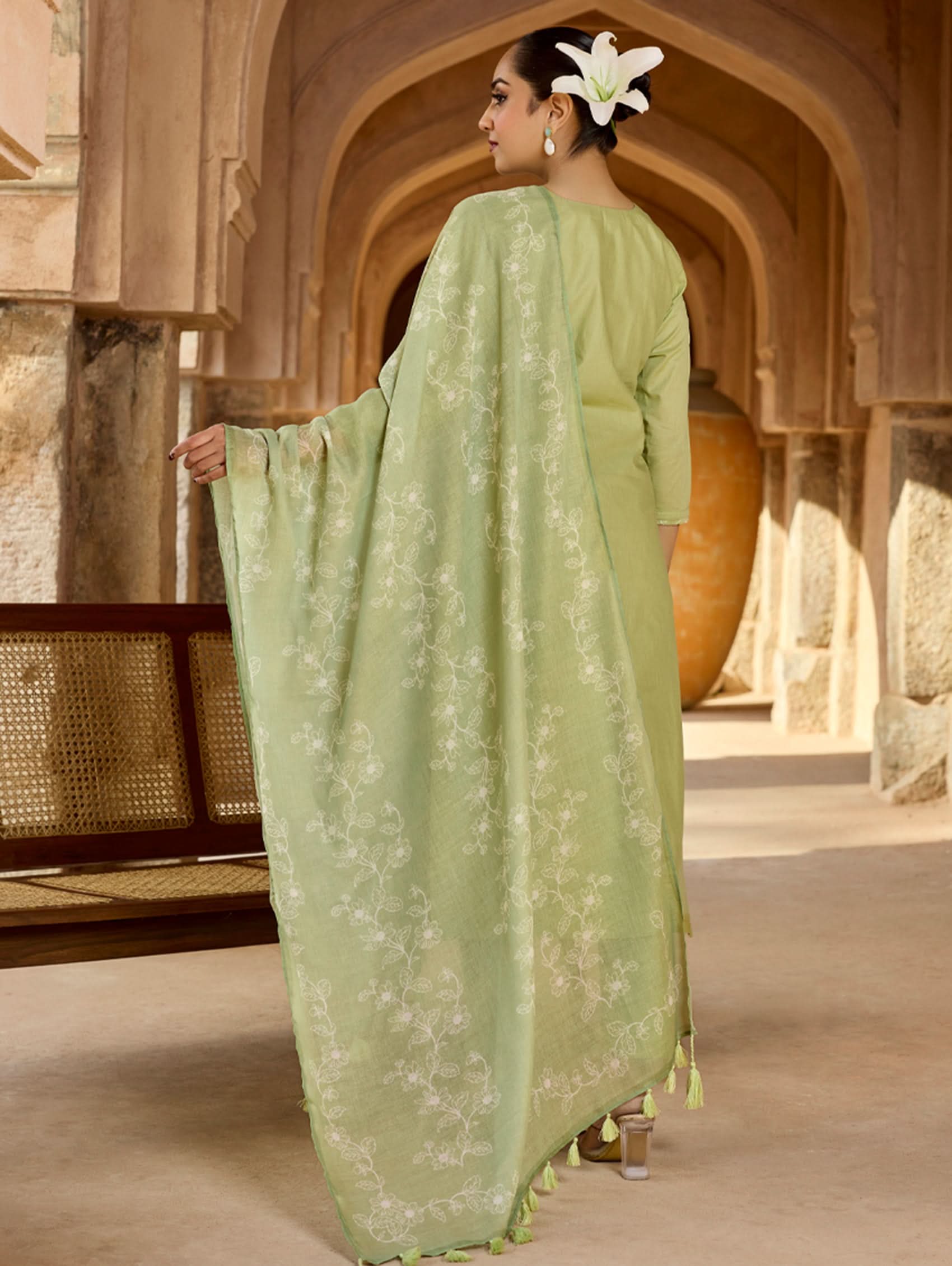 Person wearing a light green dress with floral patterns in a historical setting.