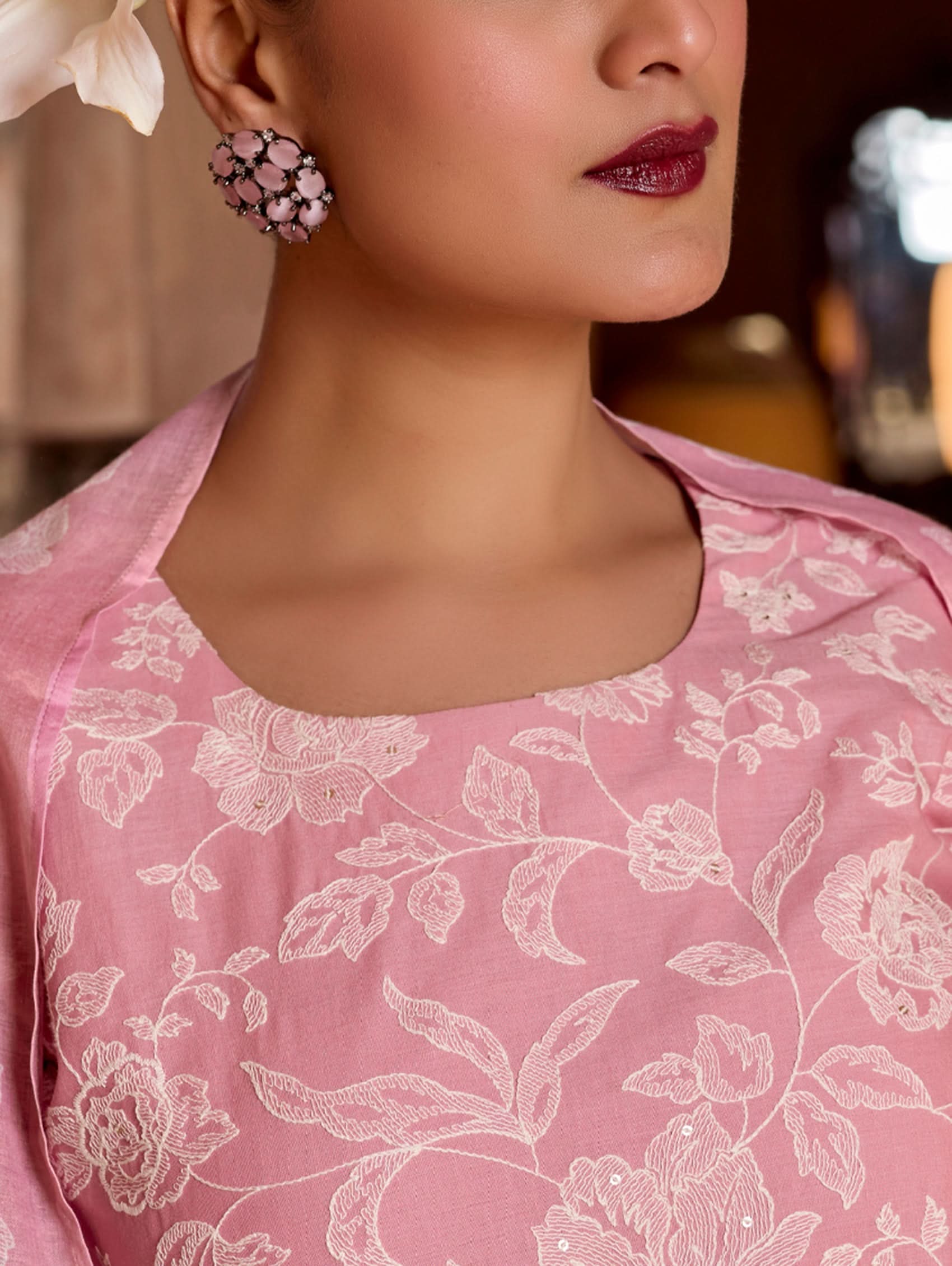 Close-up of a person wearing a pink embroidered garment with floral earrings.