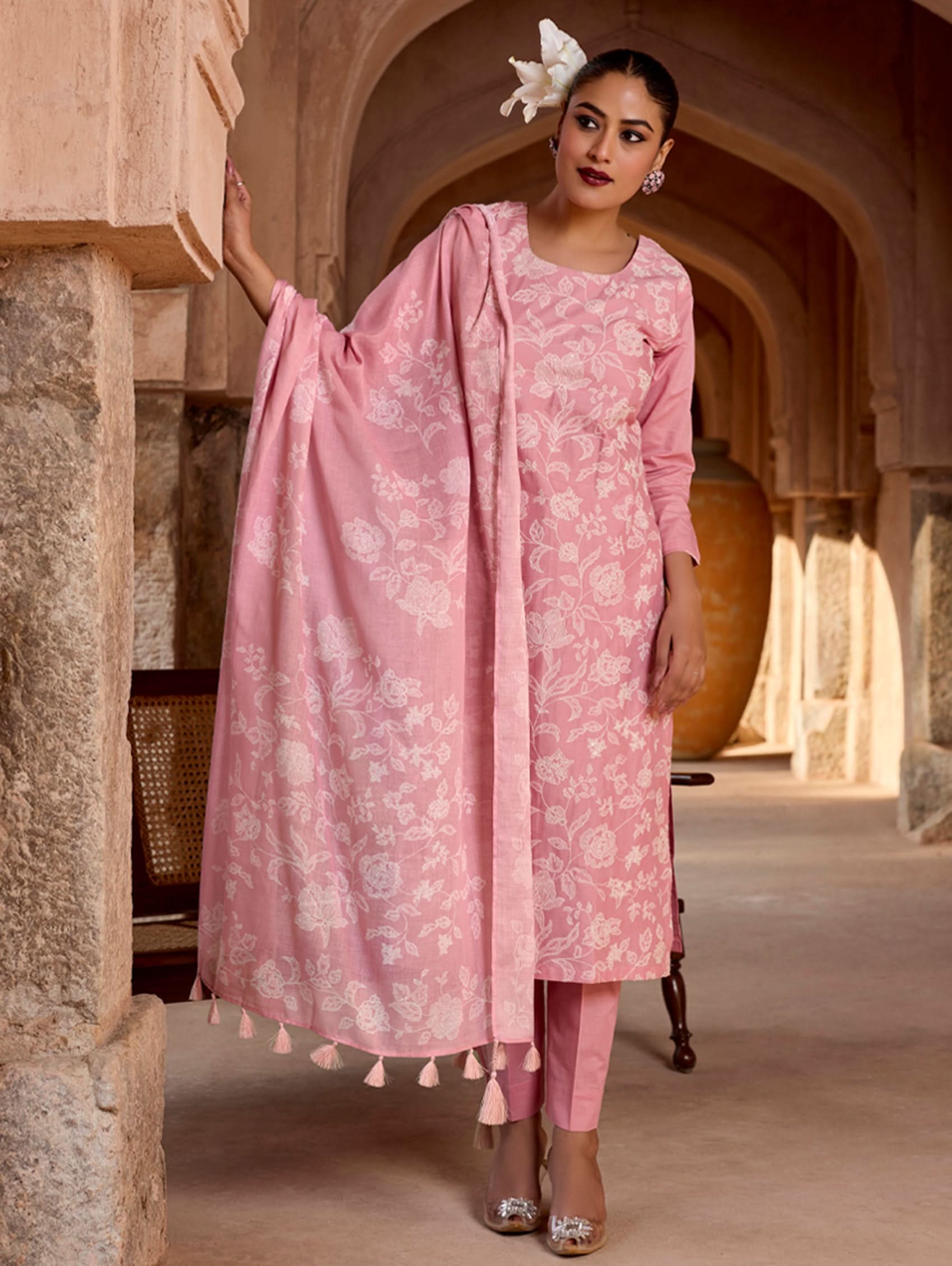 Woman in a pink traditional outfit with a dupatta in a historical setting.