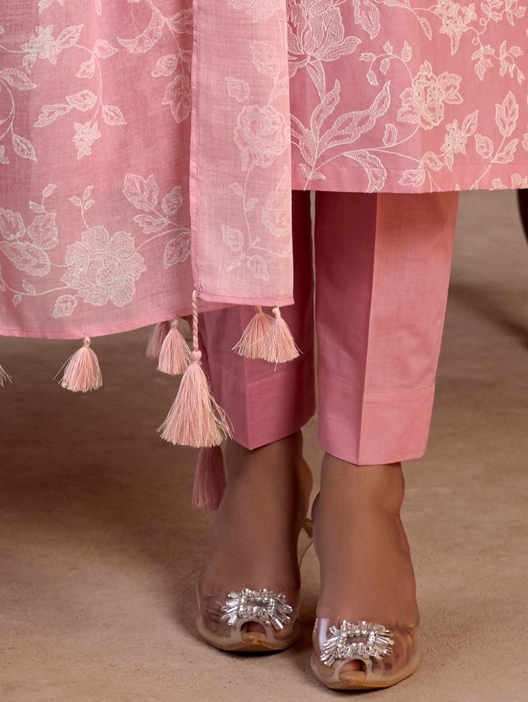 Pink embroidered garment with tassels and sandals on a neutral background