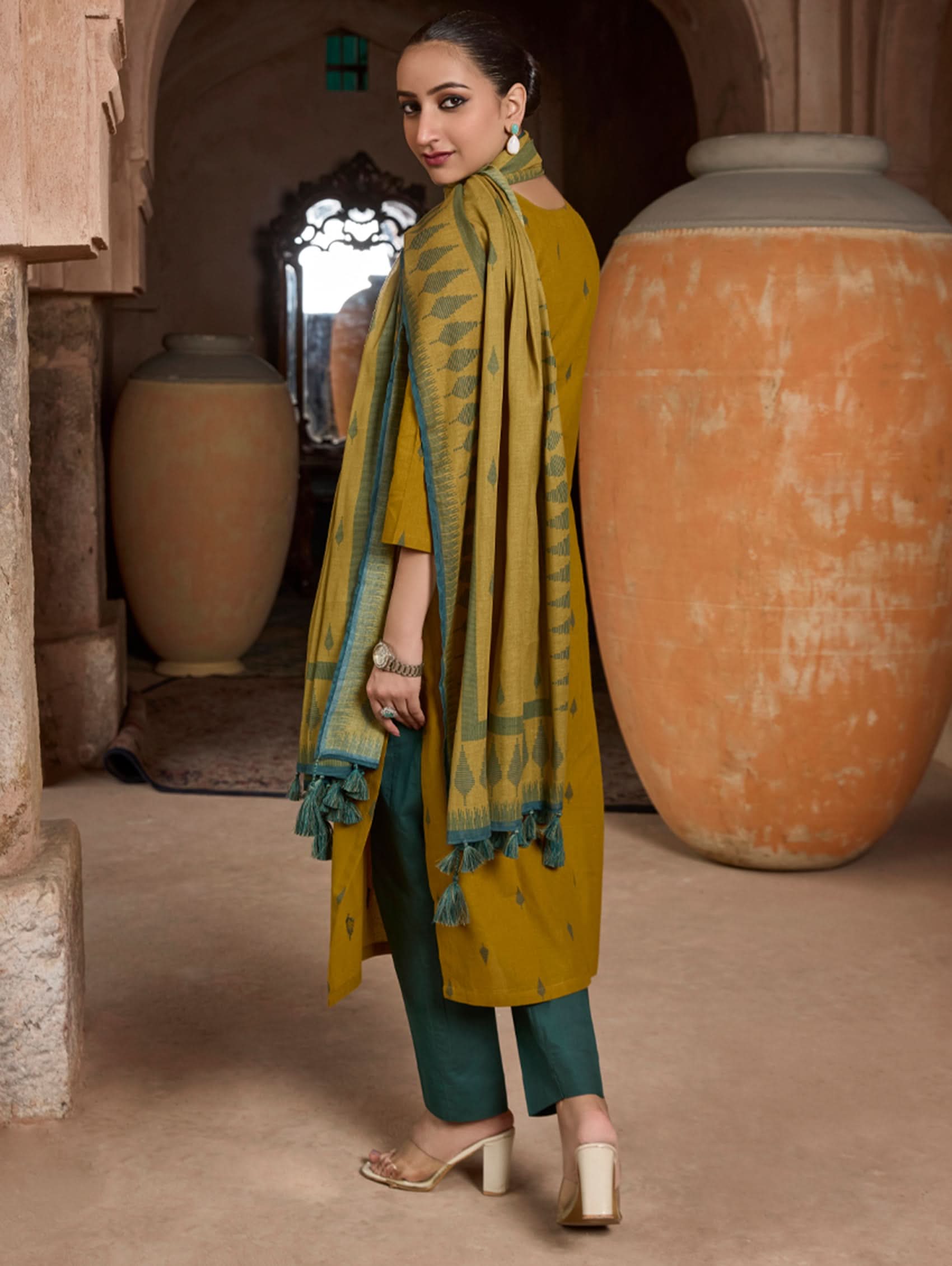 Woman in green outfit with patterned scarf in an archway with large pots.