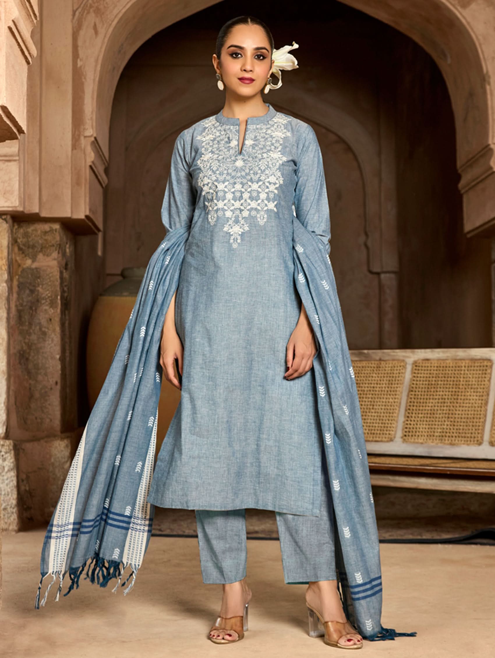 A woman modeling a blue and white pure cotton suit set with embroidery on the kurta, straight pants, and a dupatta.