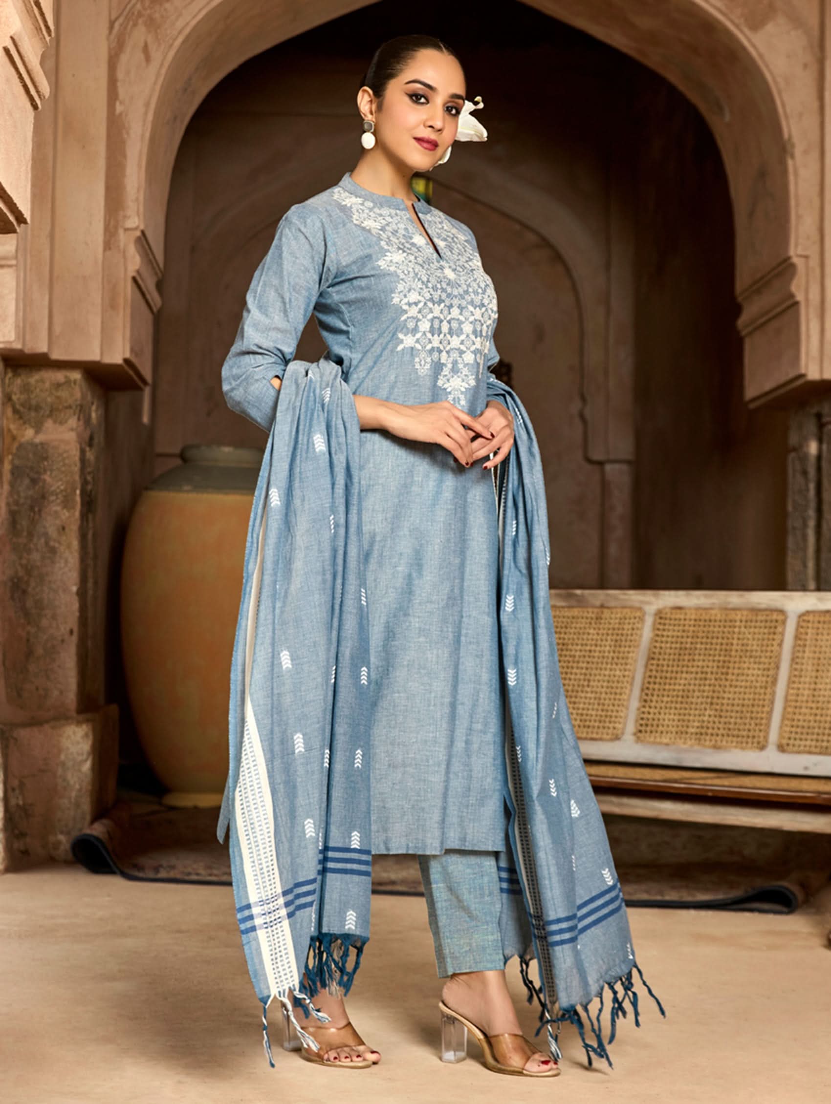Woman in a blue traditional outfit with embroidery standing in a architectural setting.
