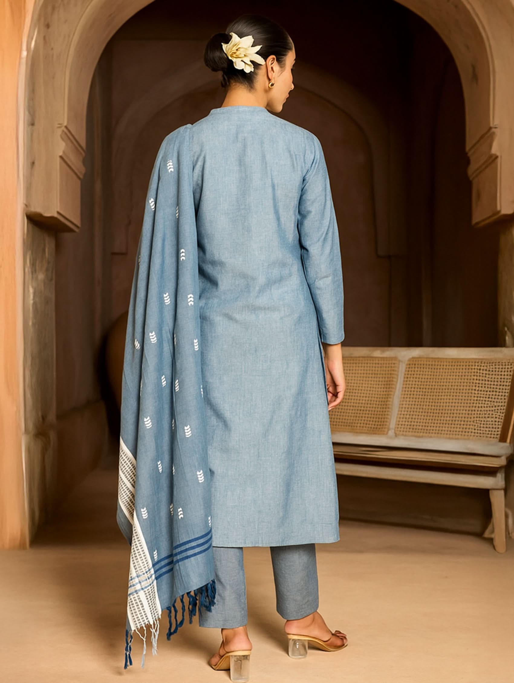 Woman in a blue traditional outfit standing in an arched doorway.