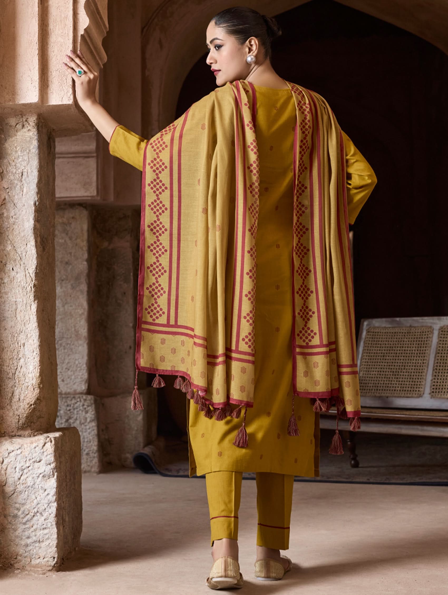 Woman in a yellow traditional outfit with a patterned shawl standing in a stone archway.