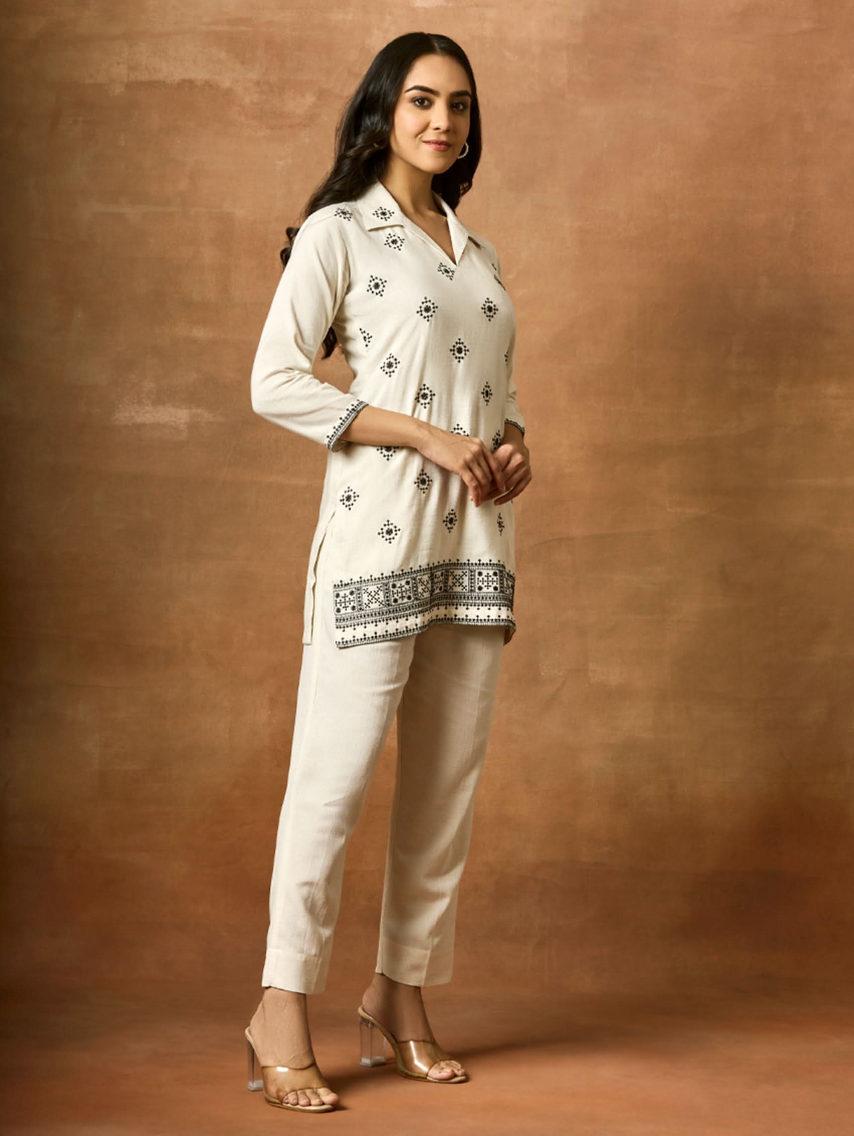 Woman wearing a white traditional outfit with black patterns against a brown background
