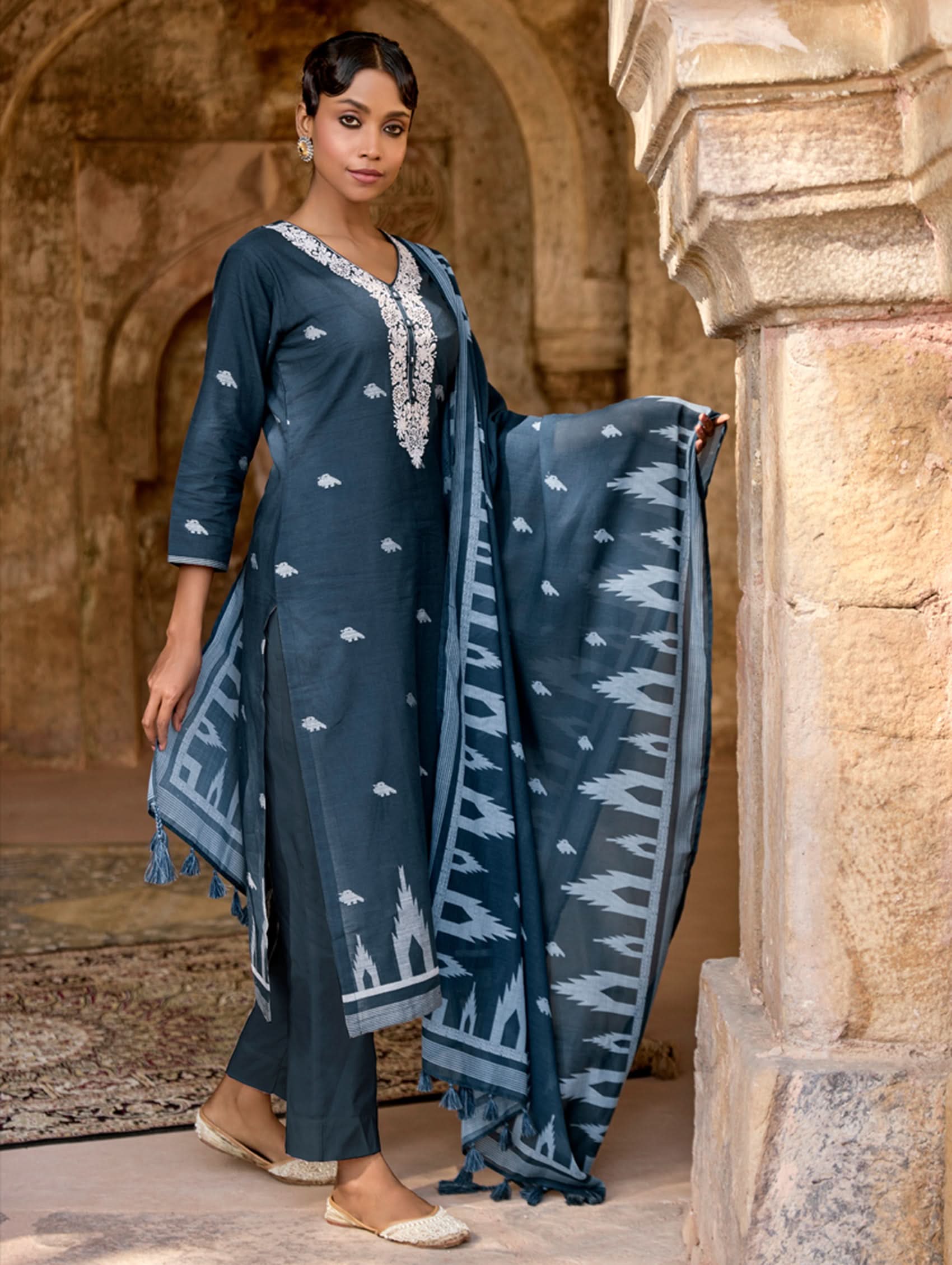 Woman in a blue traditional outfit with a patterned dupatta in an archway.