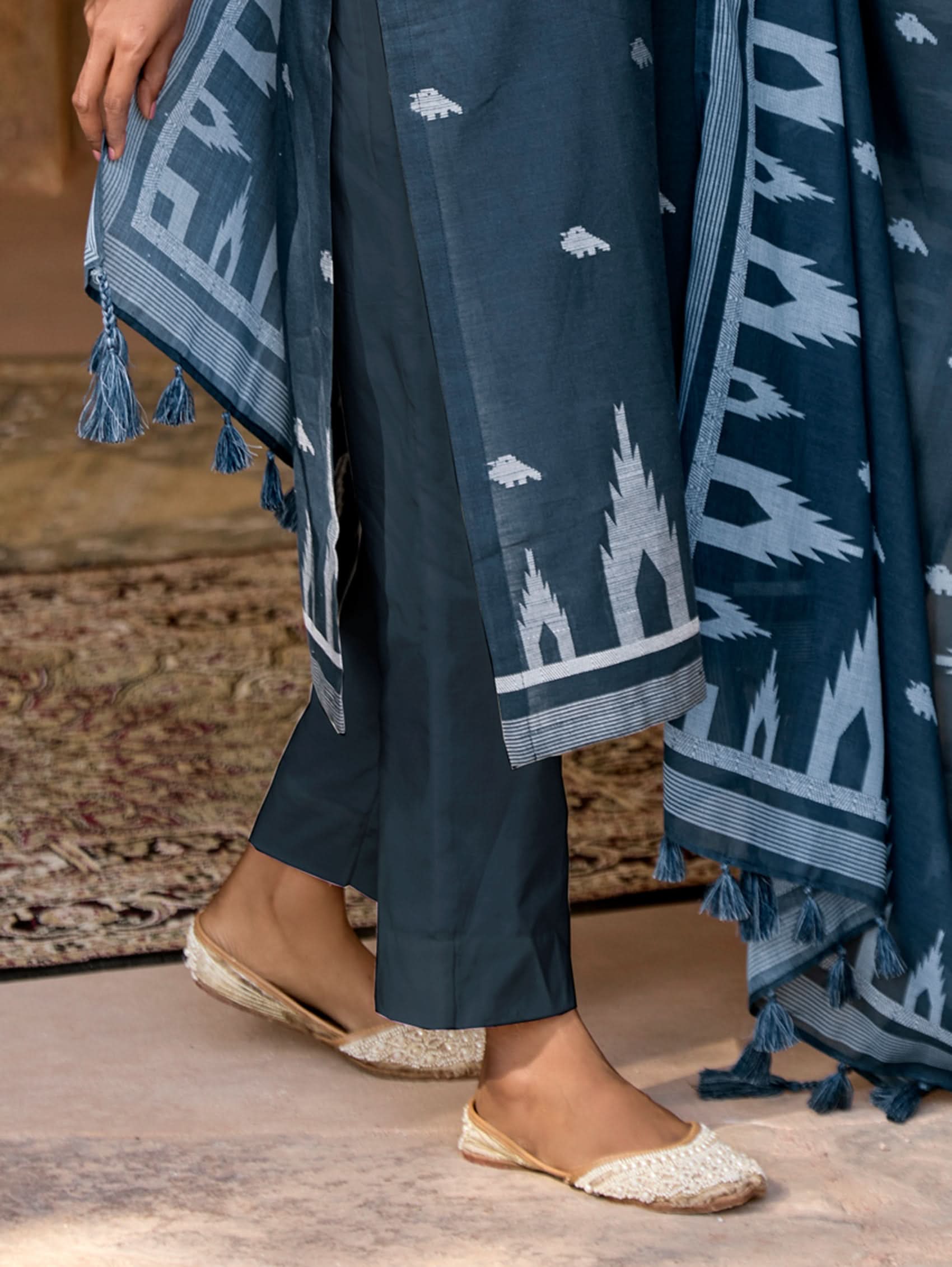 Person wearing a blue patterned shawl with tassels and dark blue pants.