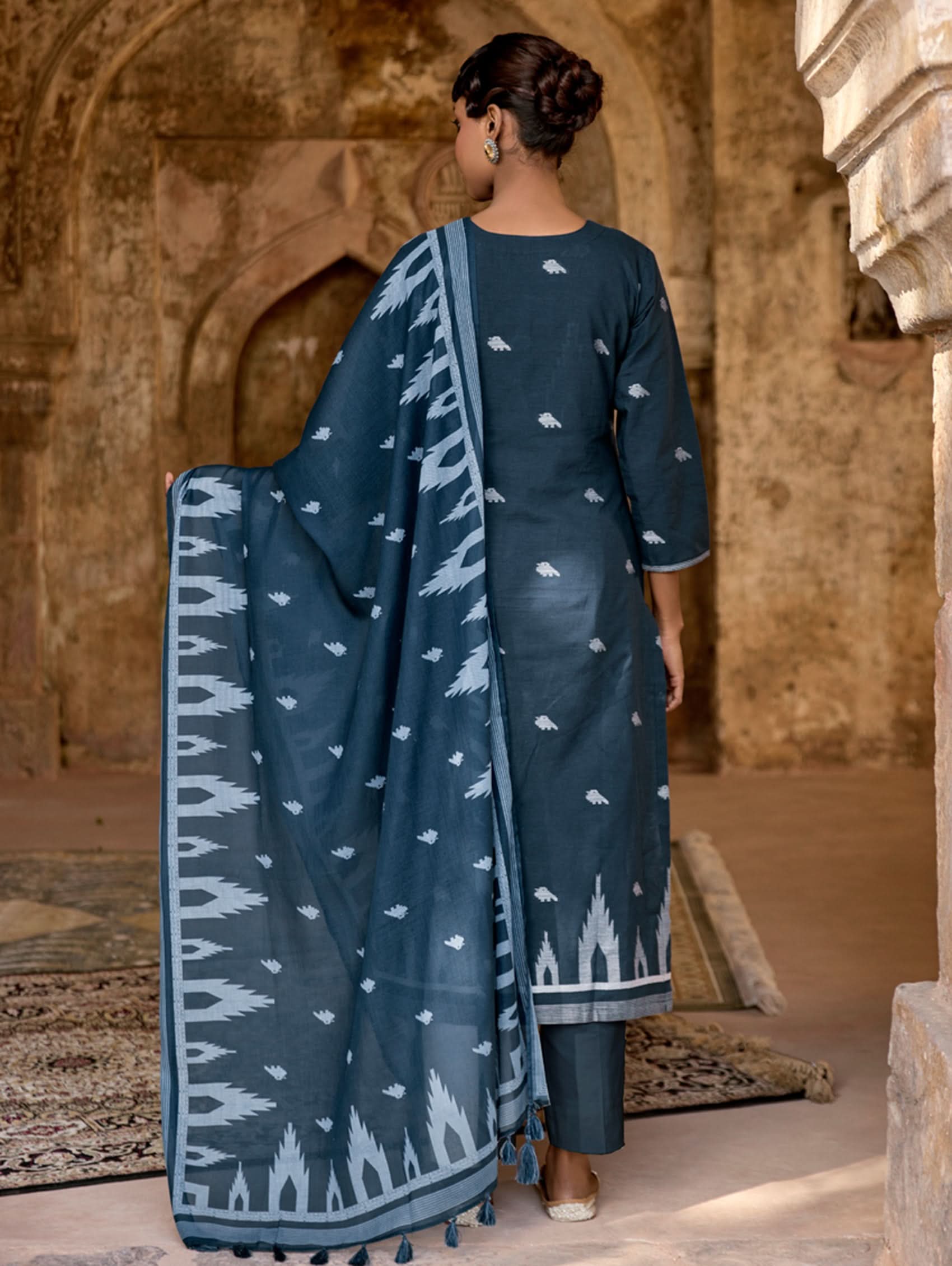 Person wearing a blue patterned saree in an architectural setting.