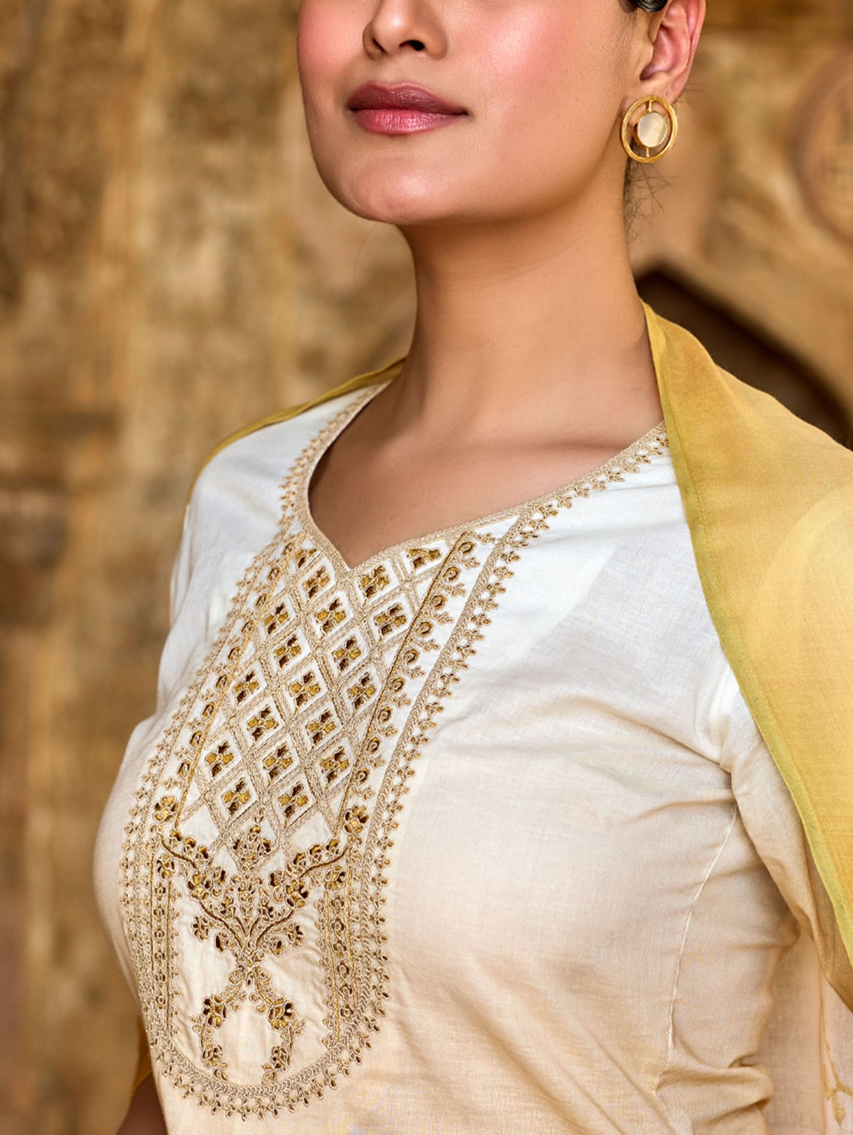 Woman wearing a white saree with gold embroidery and gold jacket against a blurred background.