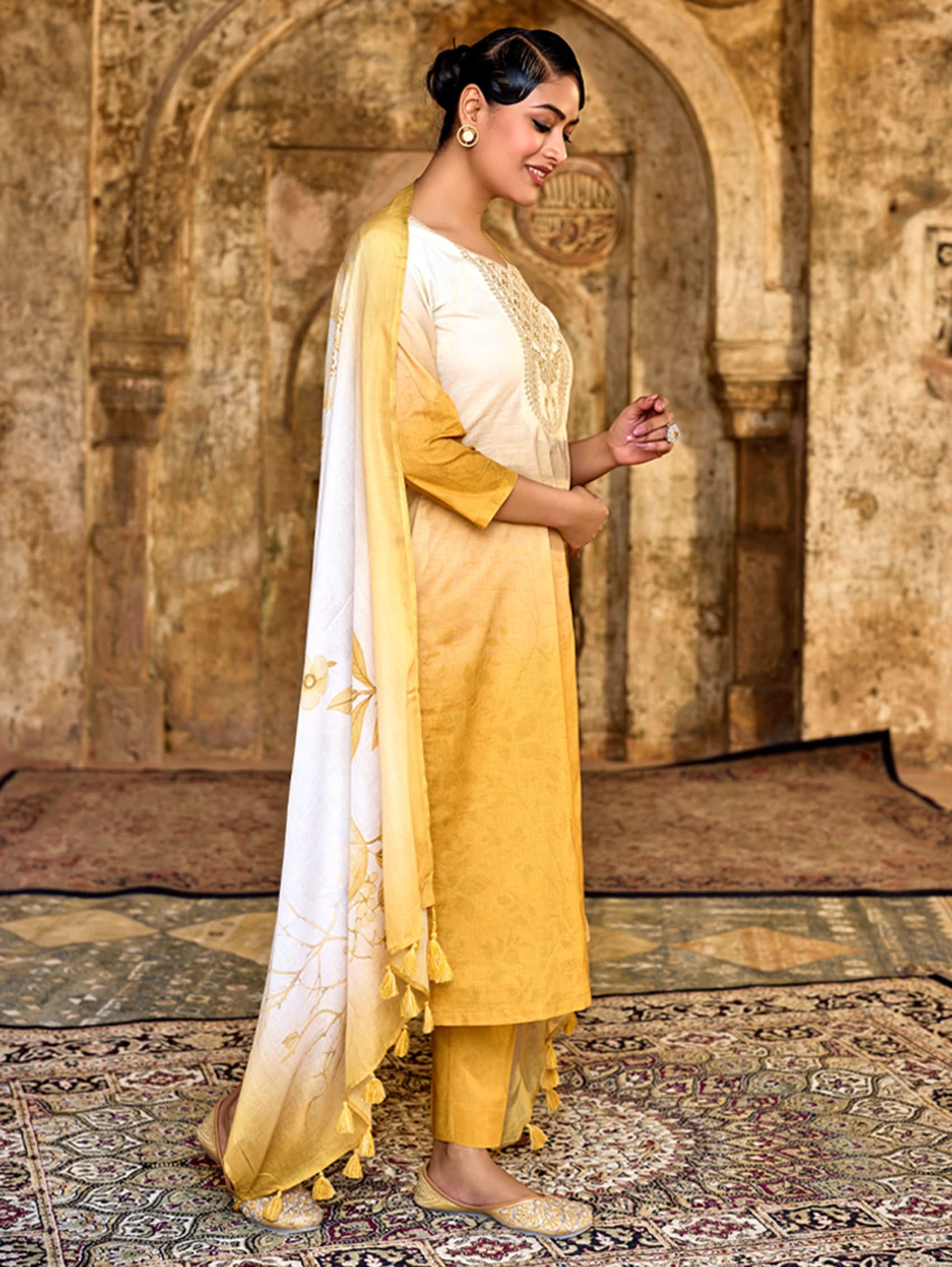 Woman in yellow traditional outfit with white dupatta in a historical setting