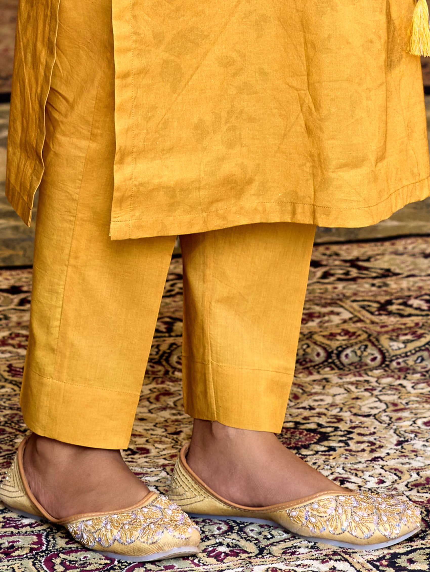 Yellow traditional outfit with embroidered shoes on a patterned carpet.