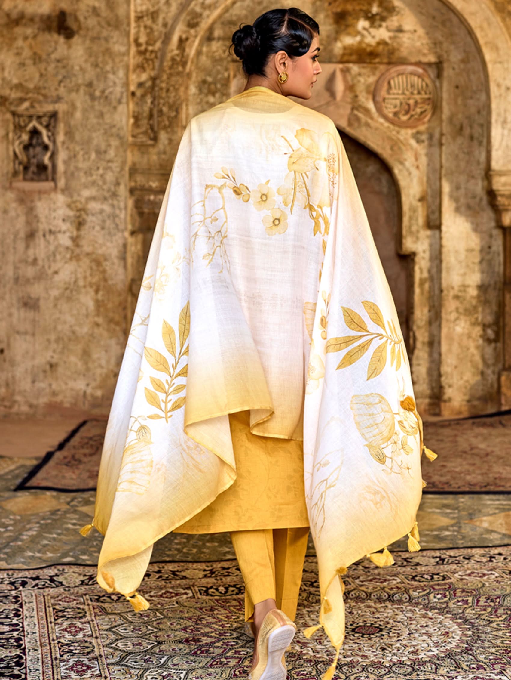 Person wearing a white and yellow embroidered shawl in a historical setting.
