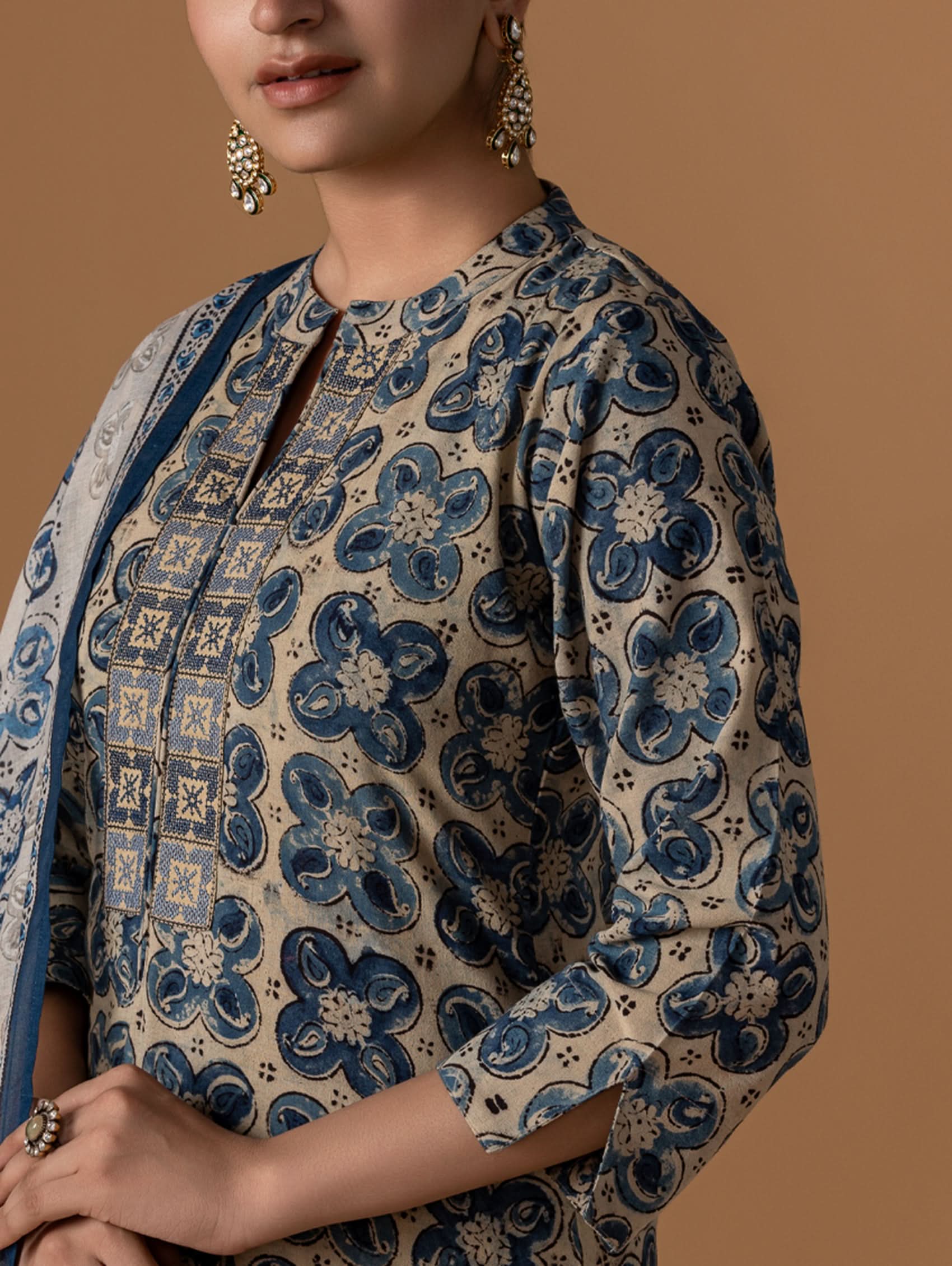 Person wearing a patterned garment with blue and beige design on a brown background.