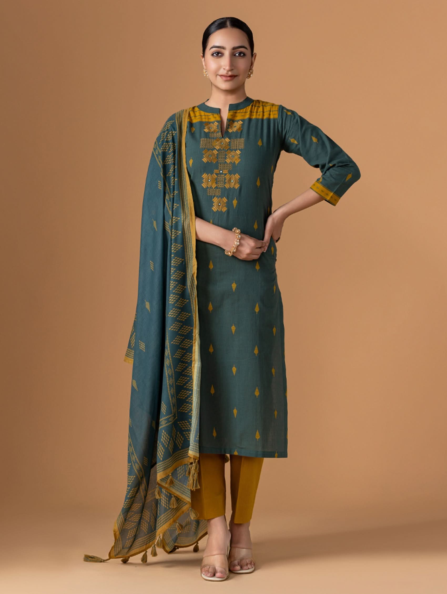 Woman wearing a green and yellow traditional outfit with a matching dupatta on a brown background