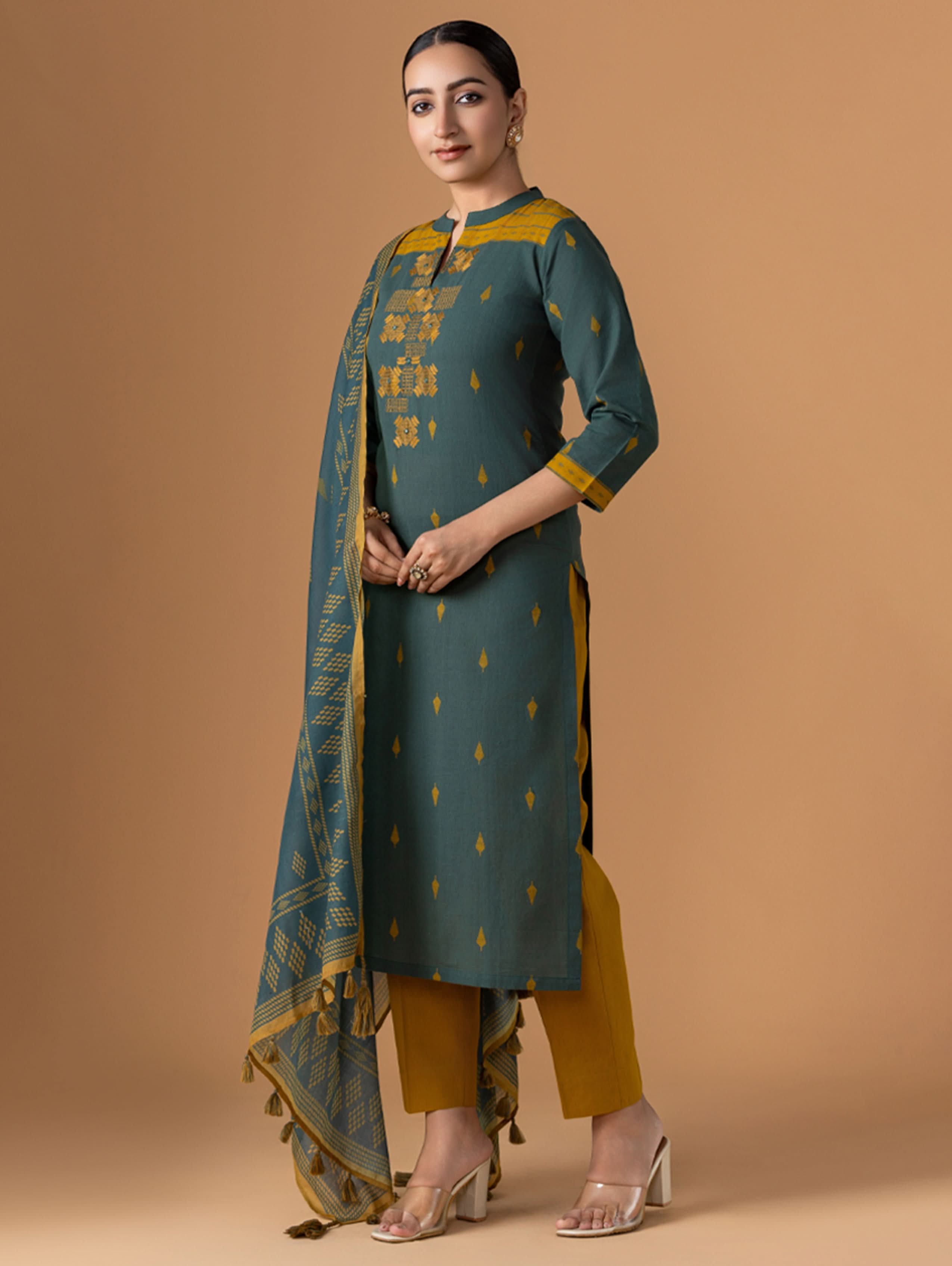 Woman wearing a green and yellow traditional outfit with a matching dupatta on a beige background