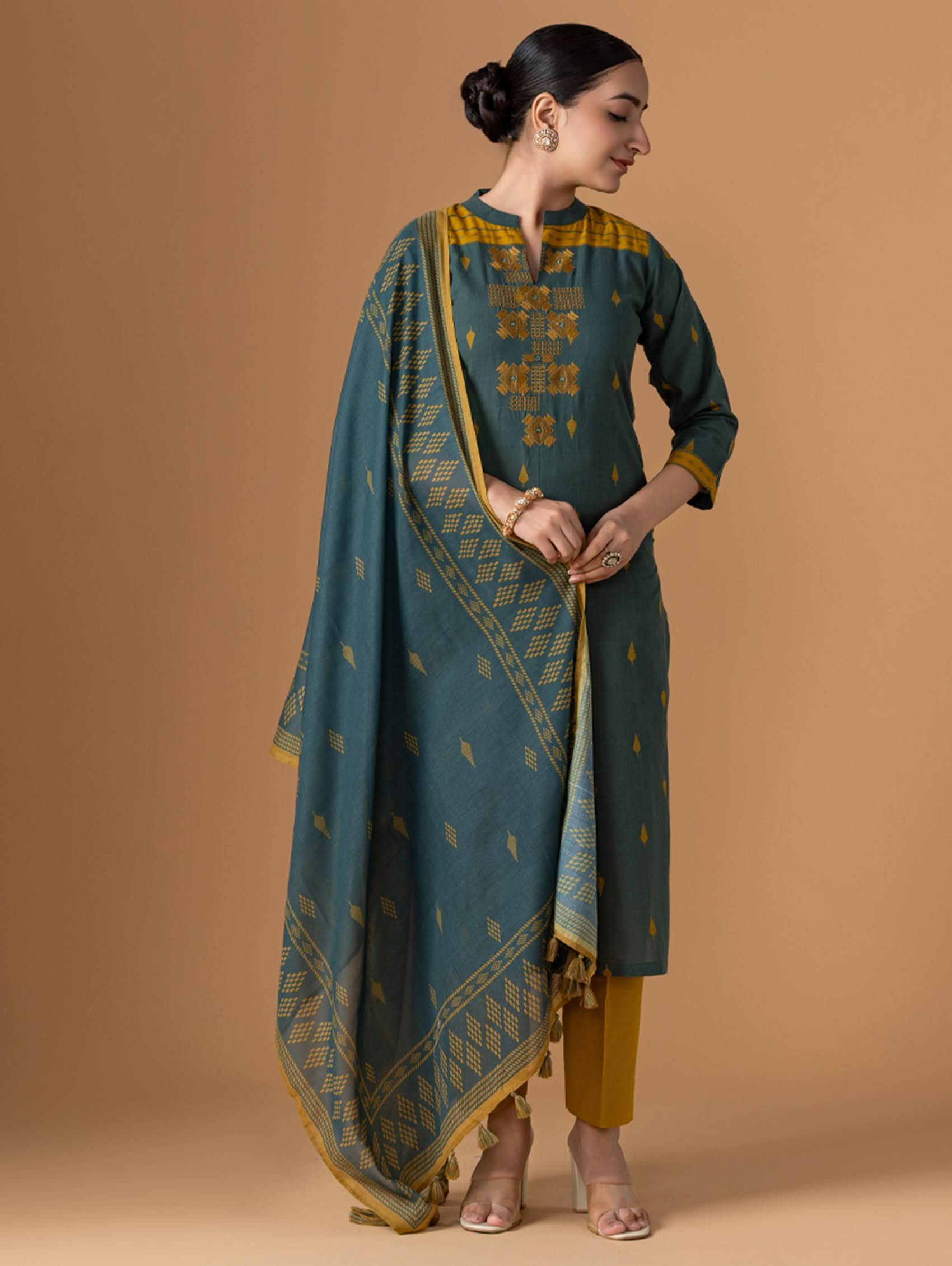 Woman wearing a teal and gold traditional outfit against a brown background