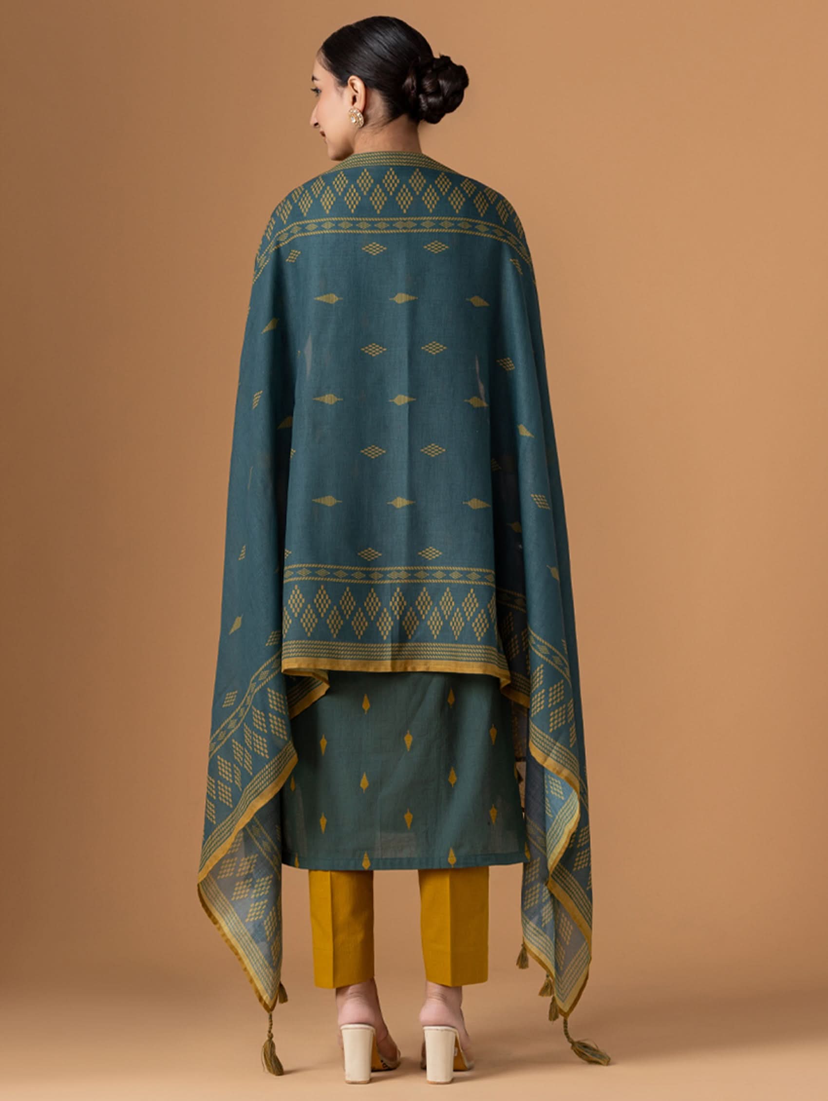 Woman wearing a green and gold traditional outfit on a beige background