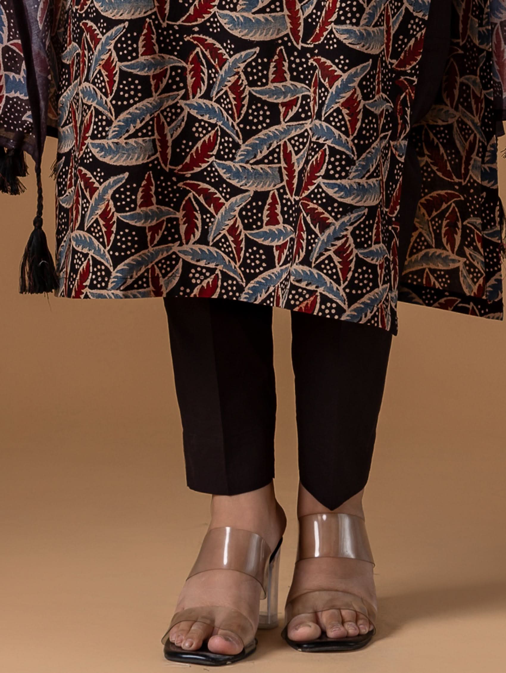 Person wearing a patterned garment with black pants and sandals on a beige background.