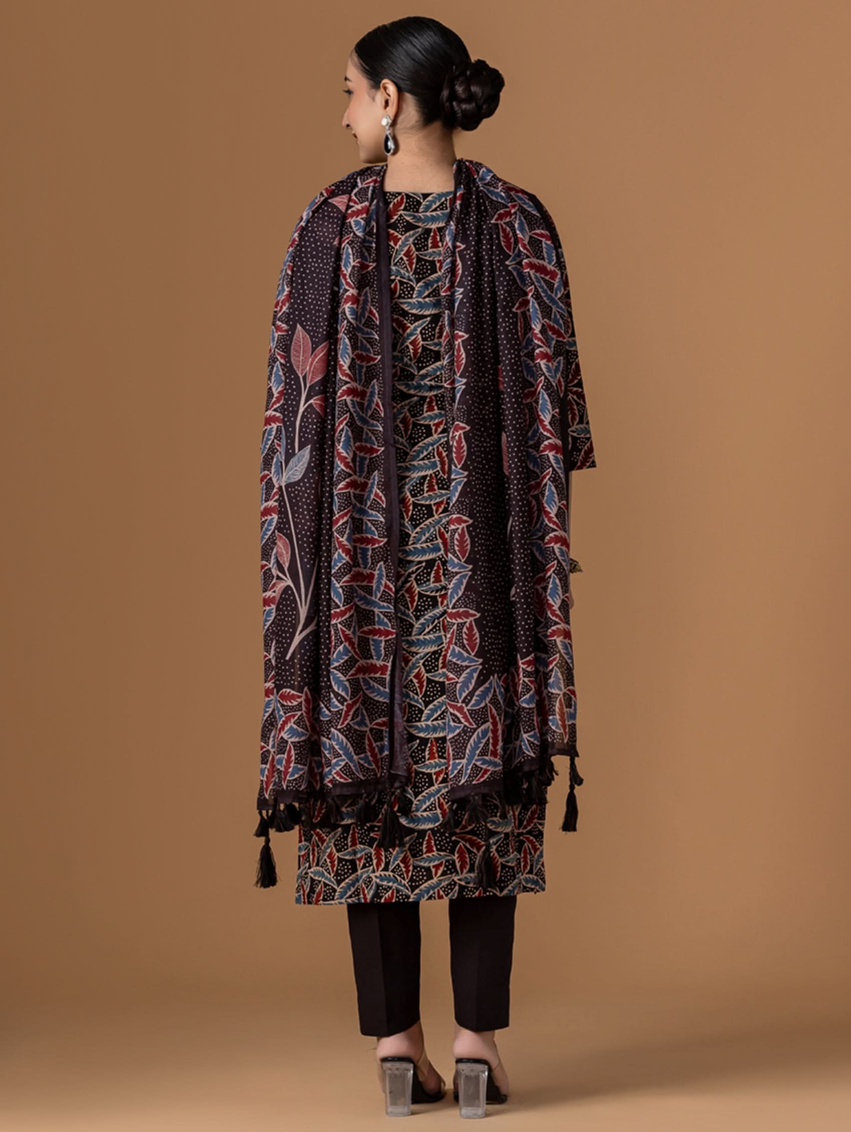 Person wearing a patterned kurta and pants on a brown background