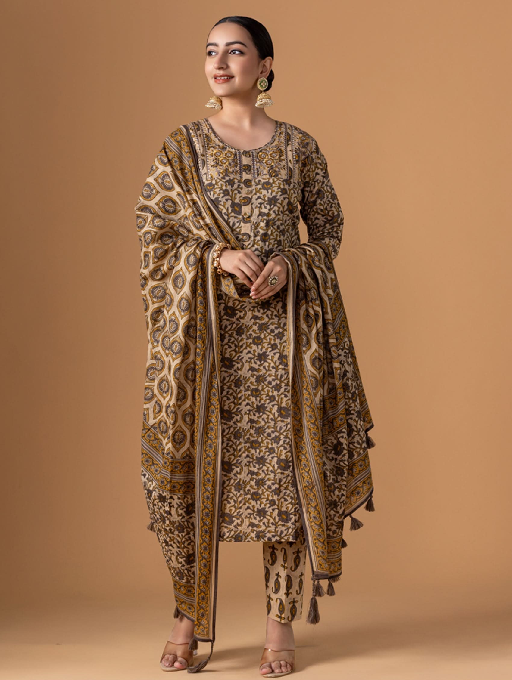 A woman wearing a traditional cotton suit set with embroidery and a dupatta, standing against a beige background.