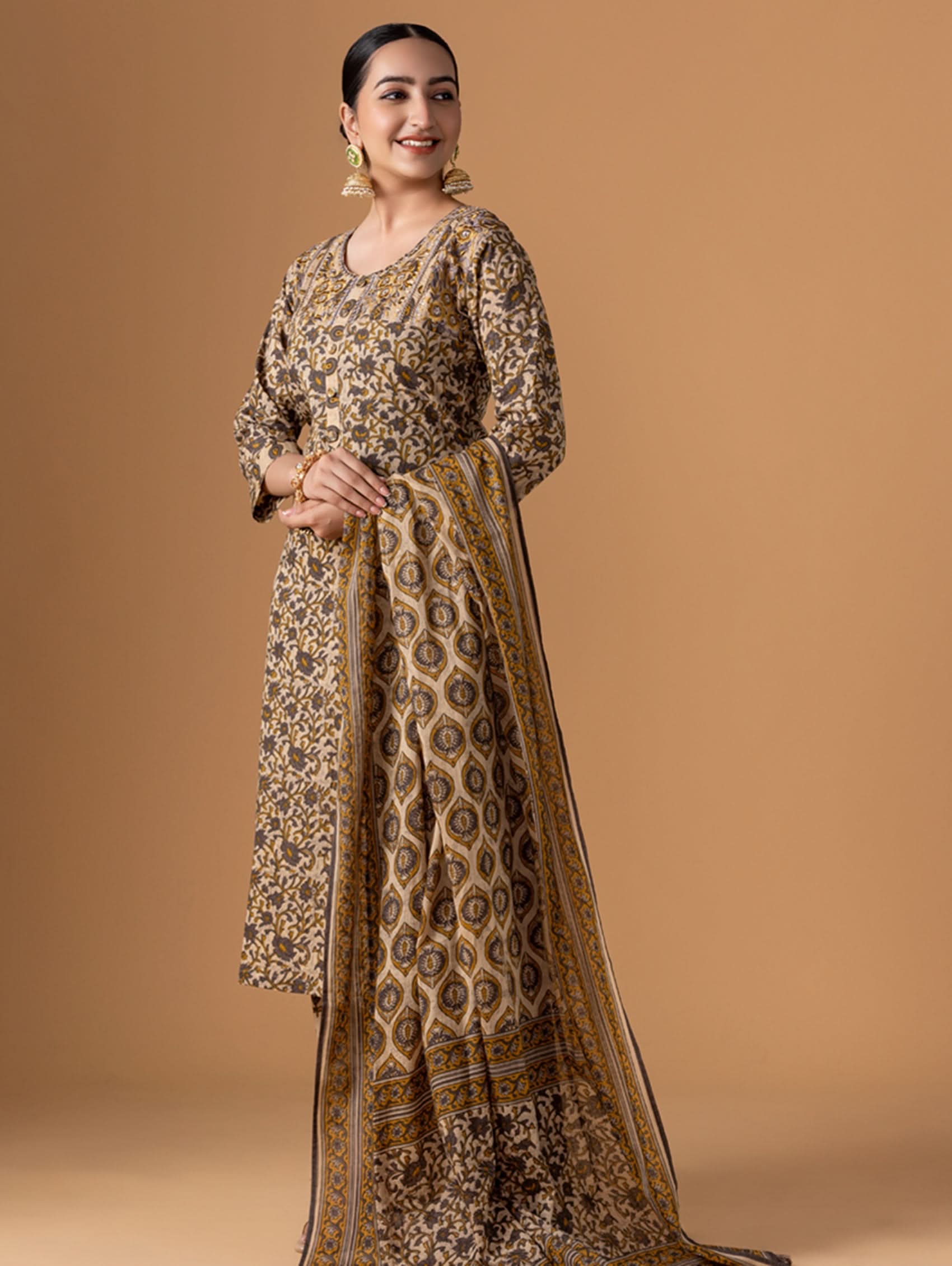 Woman wearing a patterned dress with a matching dupatta against a brown background