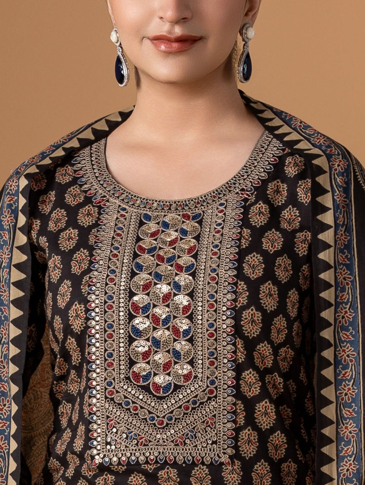 Woman wearing a black embroidered traditional outfit with intricate patterns on a beige background