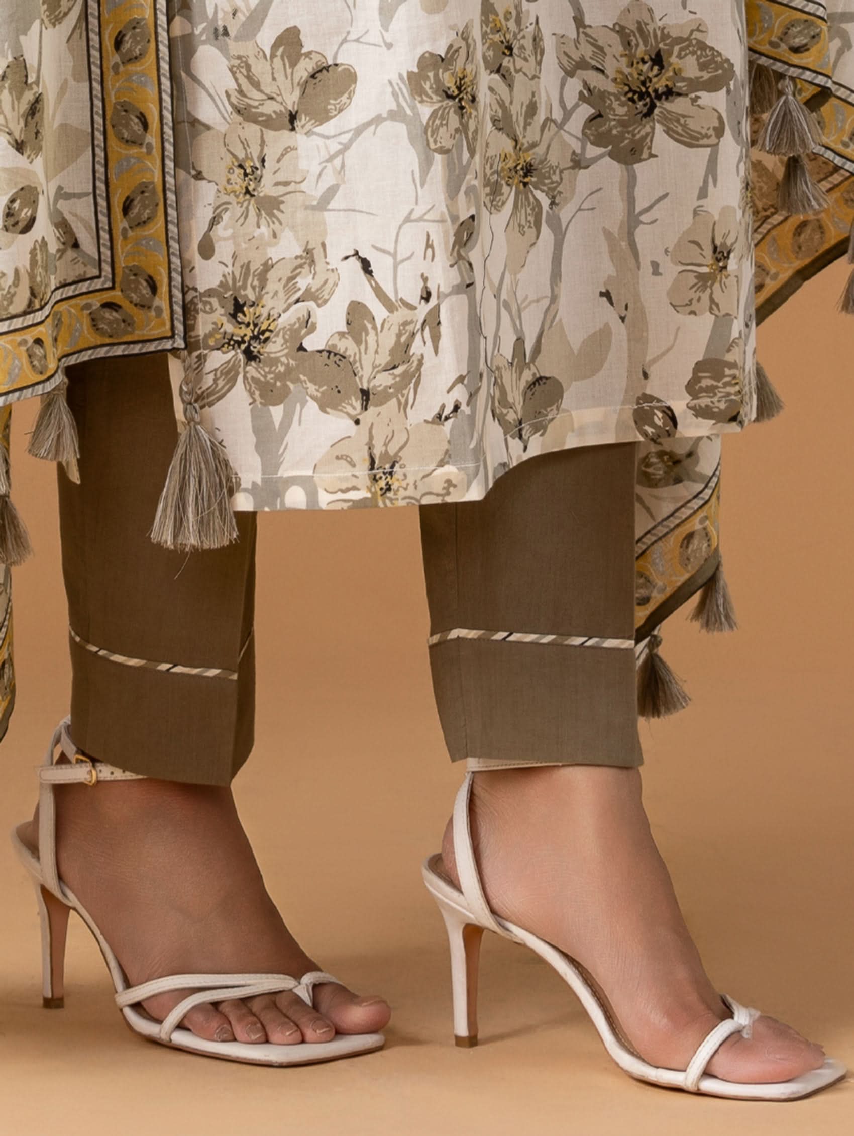 Close-up of a person wearing floral pants and high-heeled sandals on a beige background