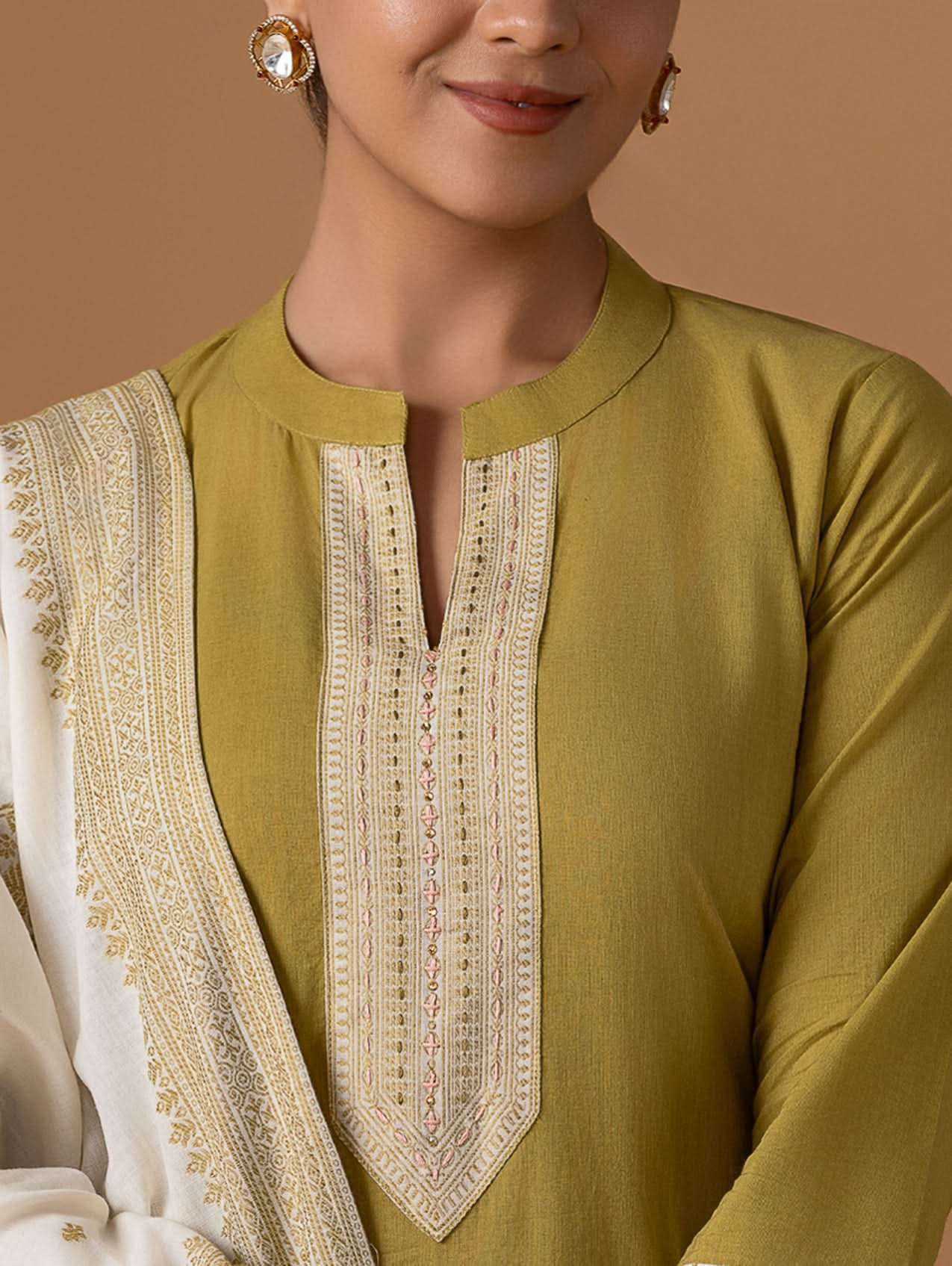 Close-up of a green kurta with lace detailing on a person against a brown background.