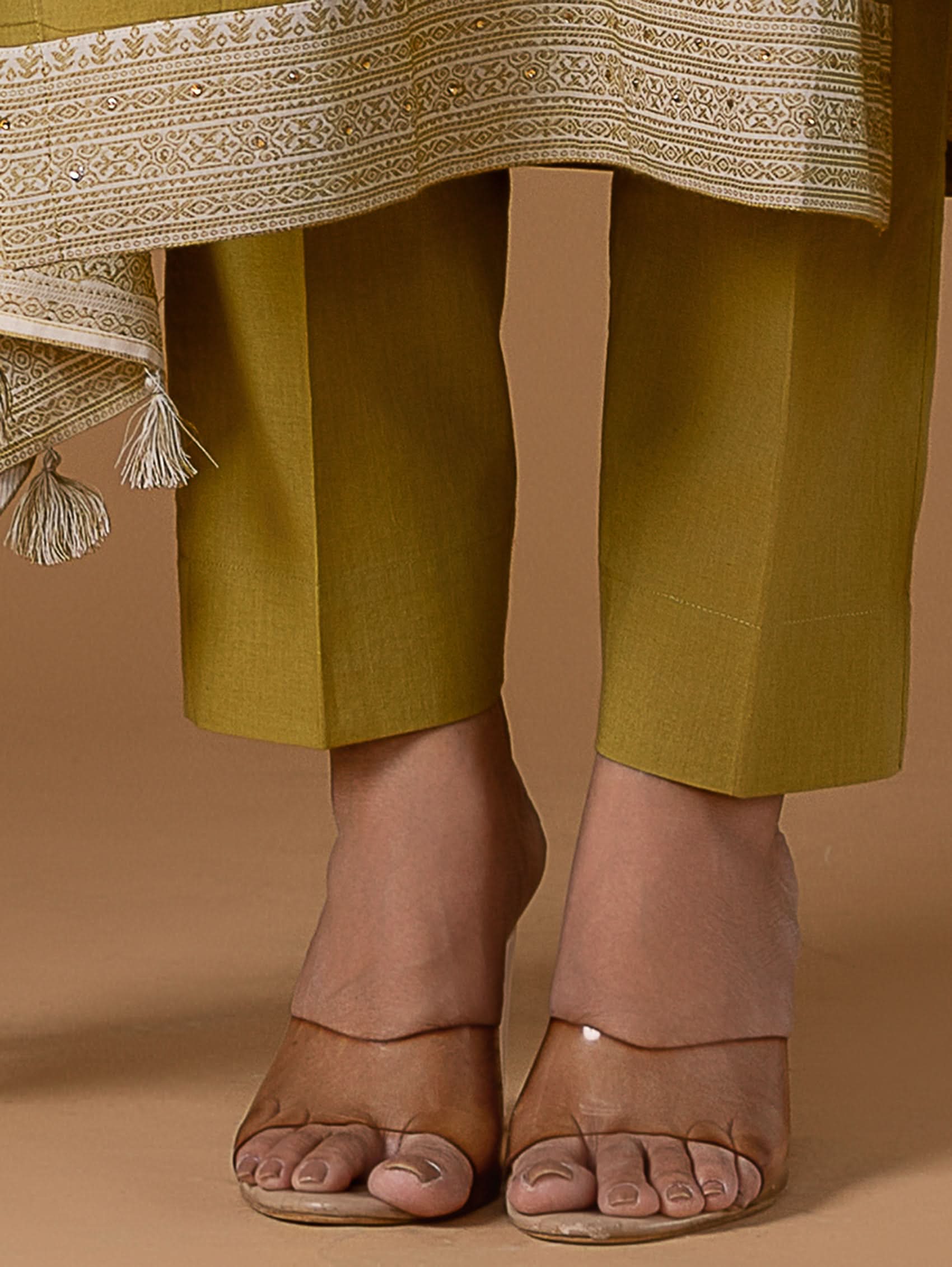 Green pants with a patterned shawl and transparent sandals on a brown background