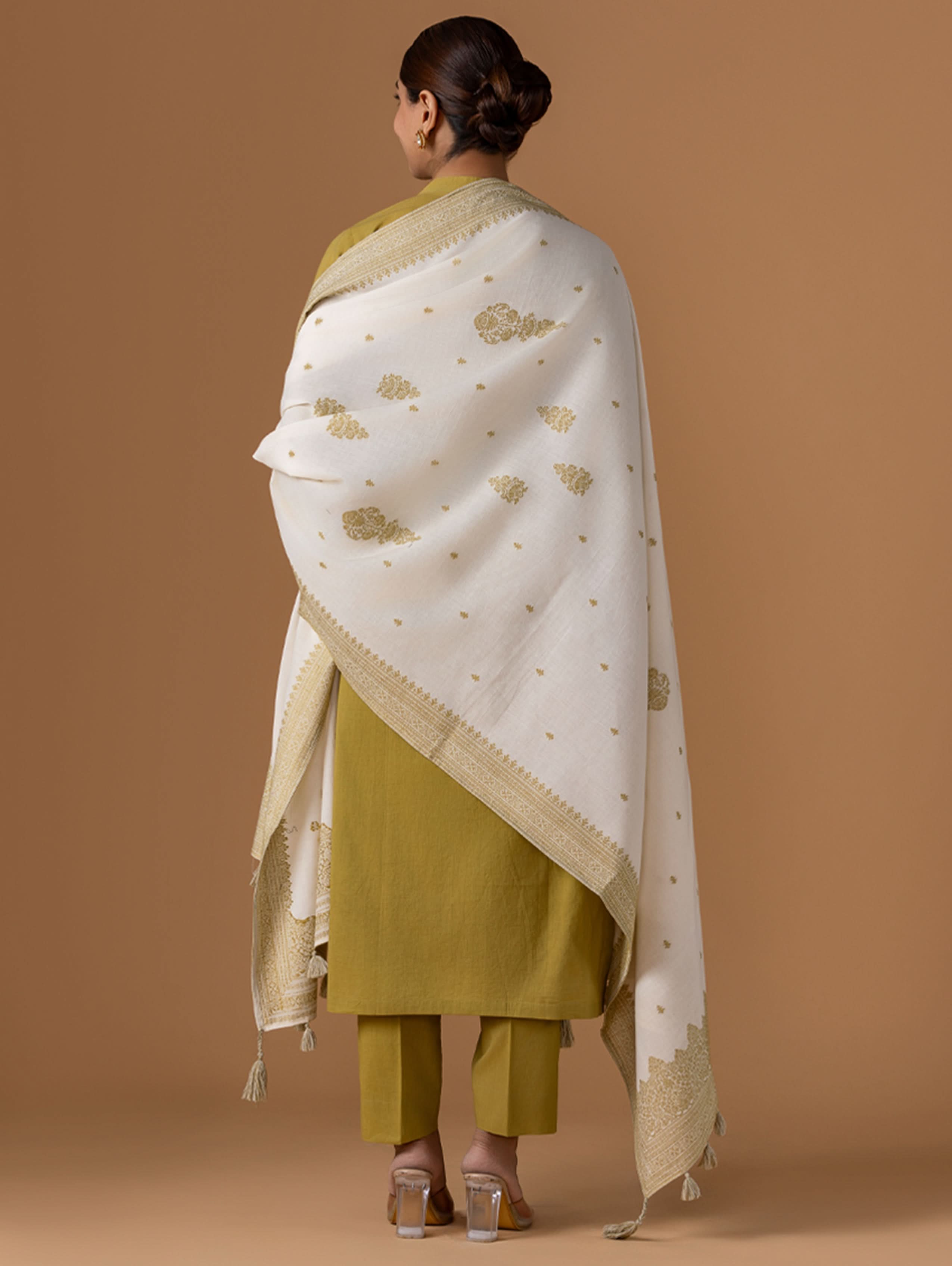 Woman wearing a white and gold patterned shawl over a green outfit on a brown background.