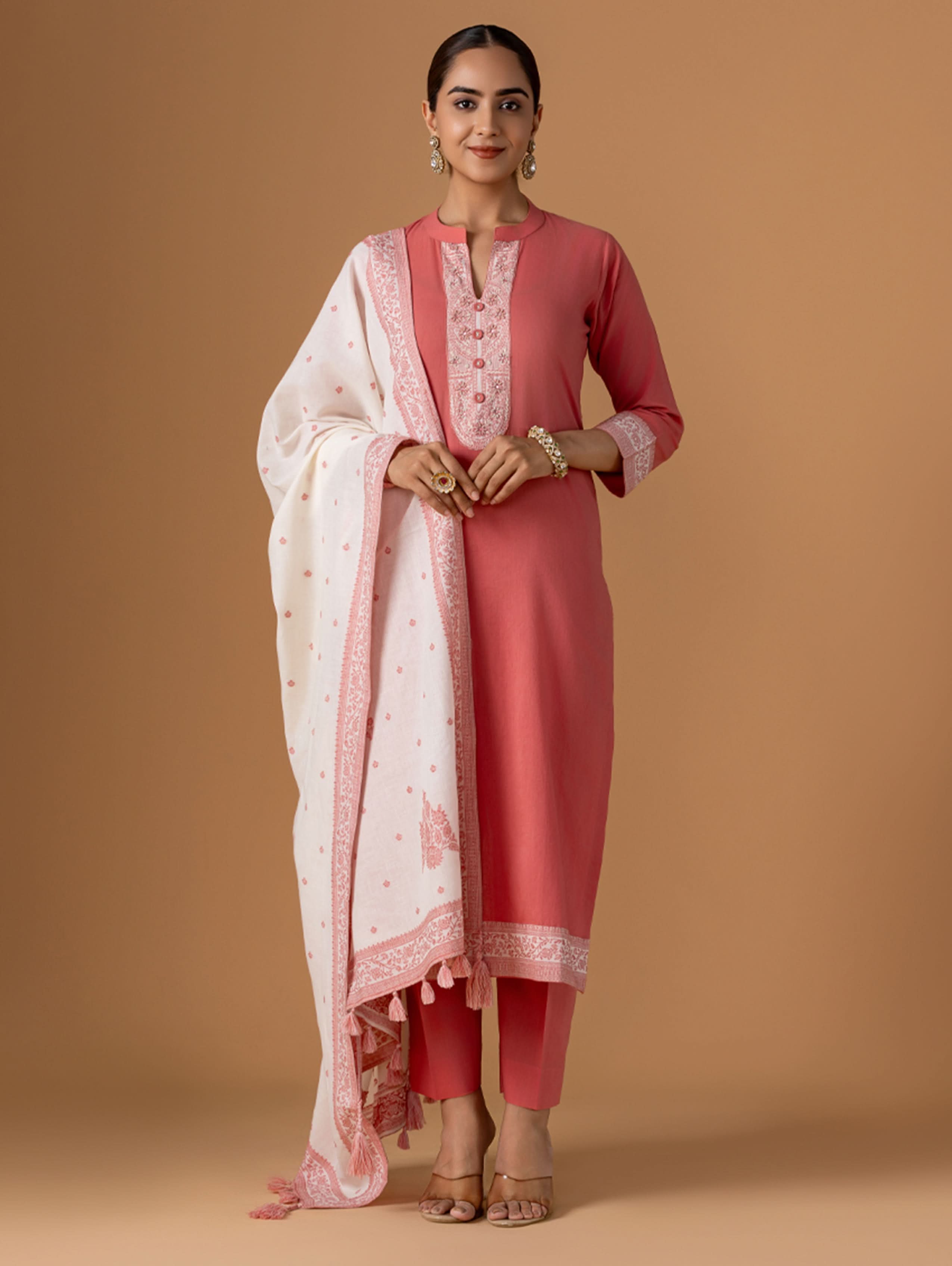 Woman wearing a pink traditional outfit with a white dupatta on a beige background