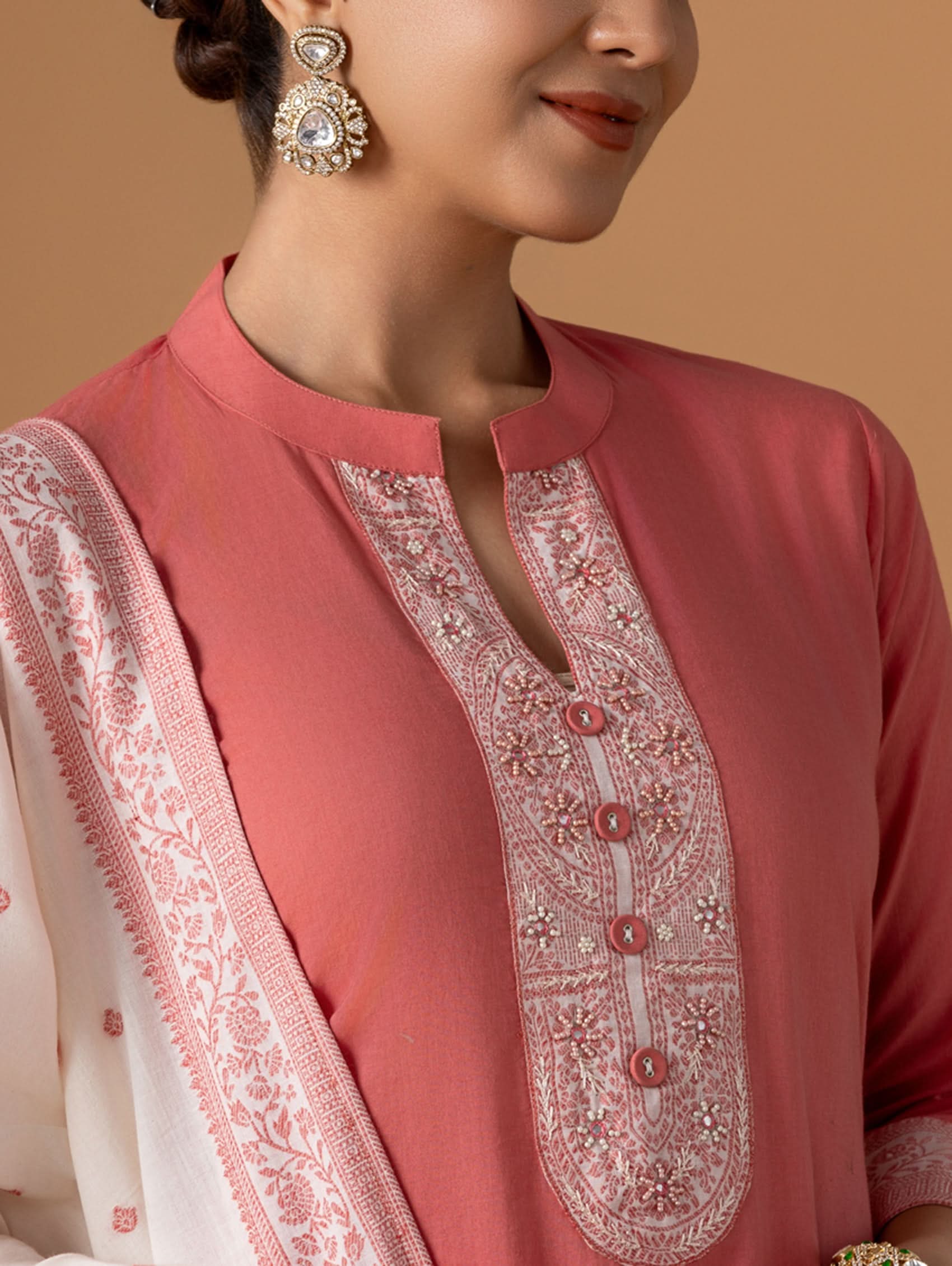 Close-up of a person wearing a pink embroidered outfit with a beige background