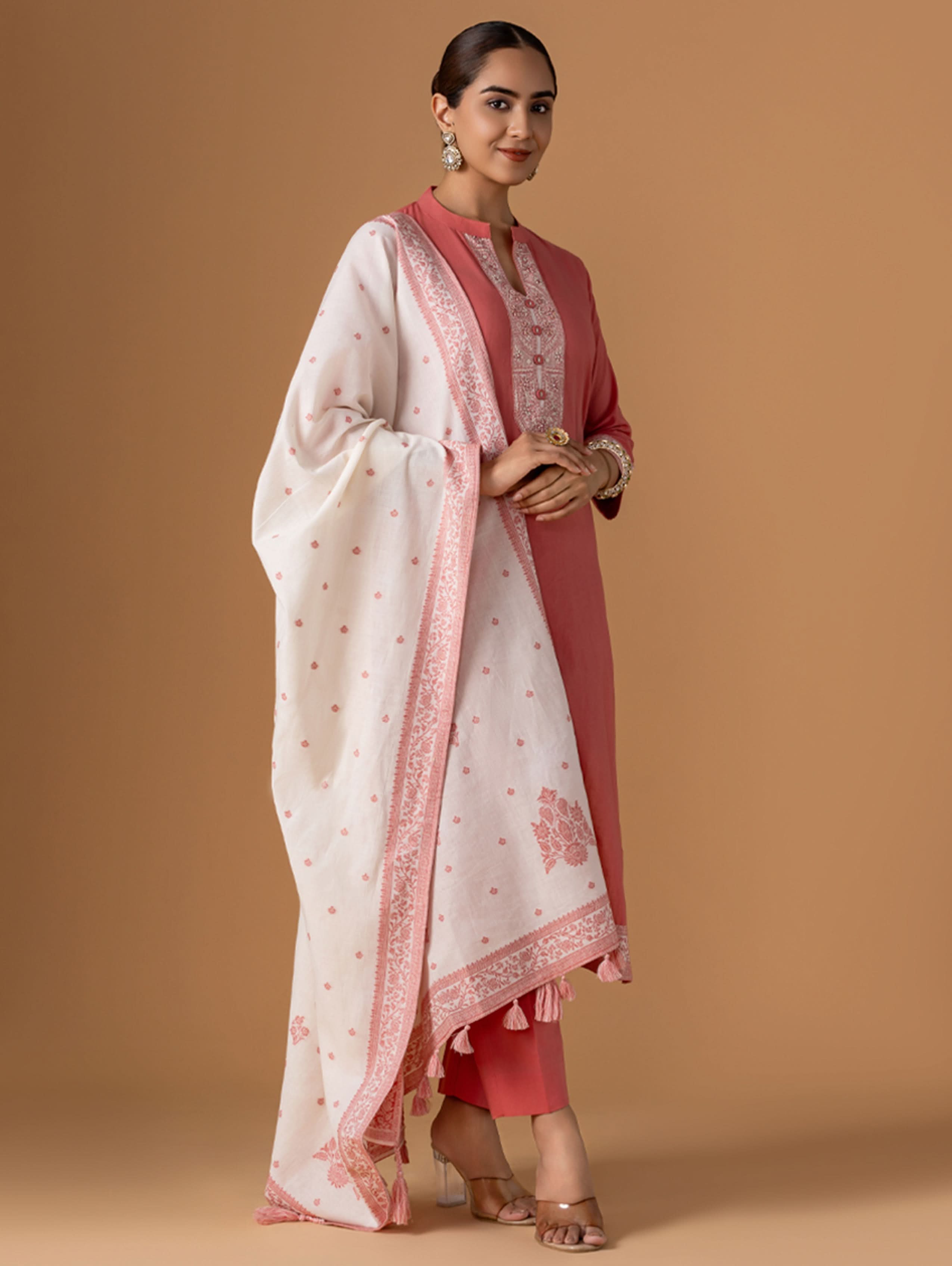 Woman wearing a traditional outfit with a white dupatta and pink kurta against a brown background