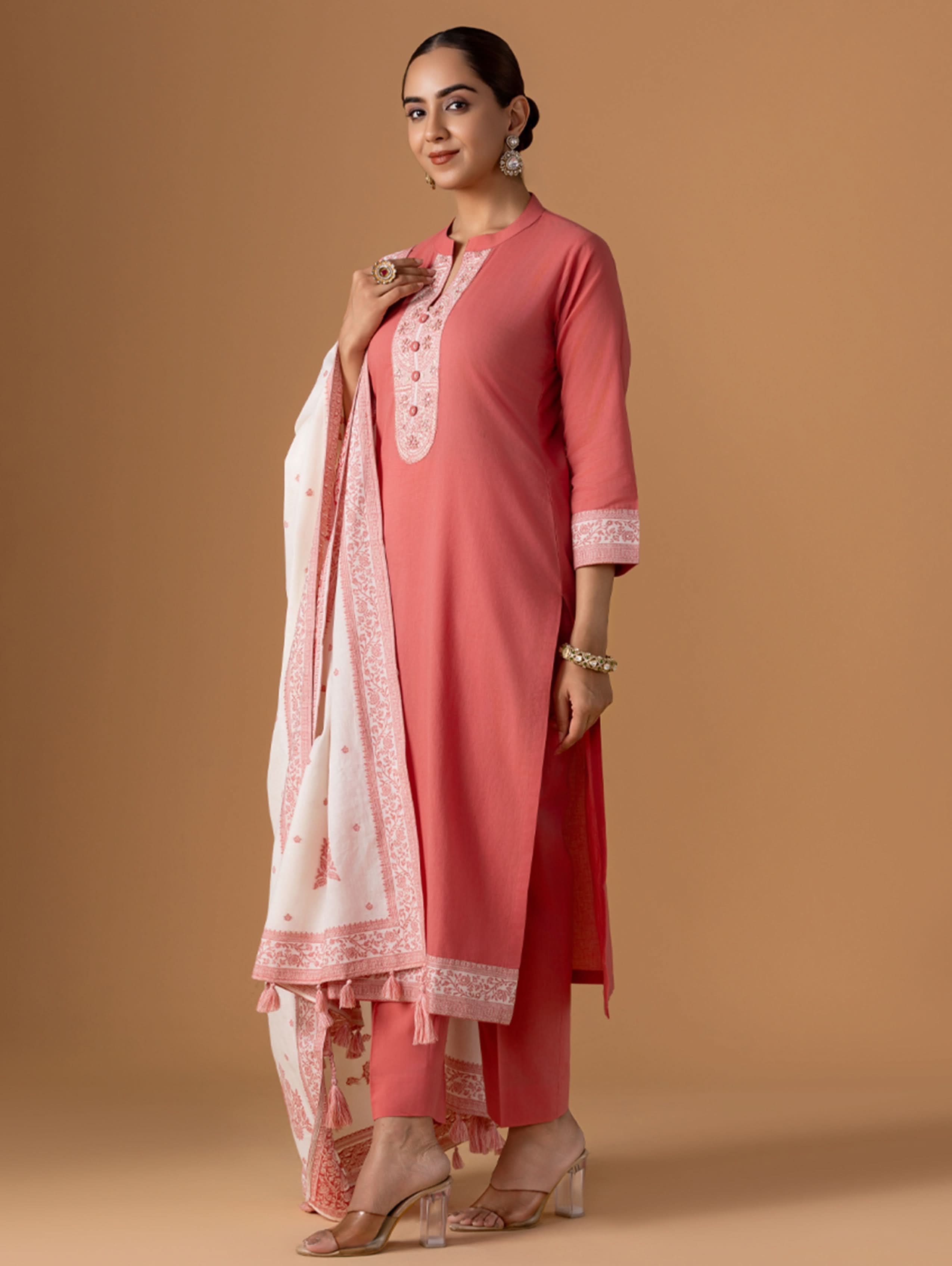 Woman wearing a pink traditional outfit with a matching dupatta against a brown background
