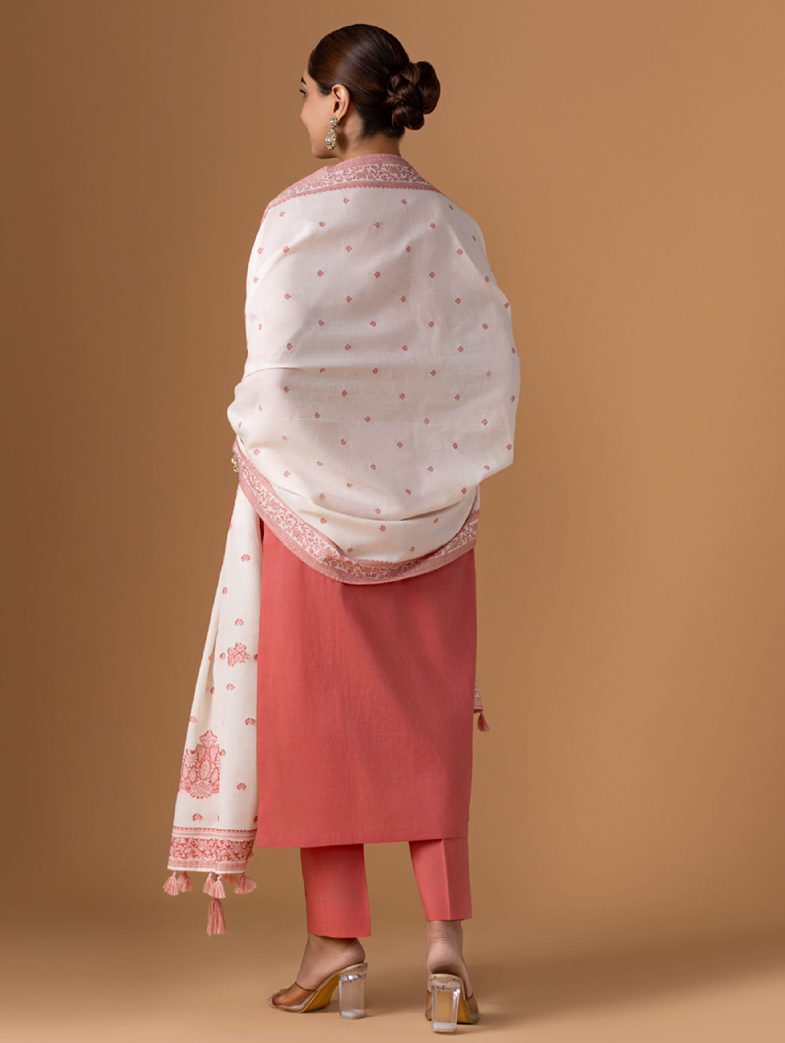 Woman wearing a white and pink traditional outfit with a matching dupatta on a brown background