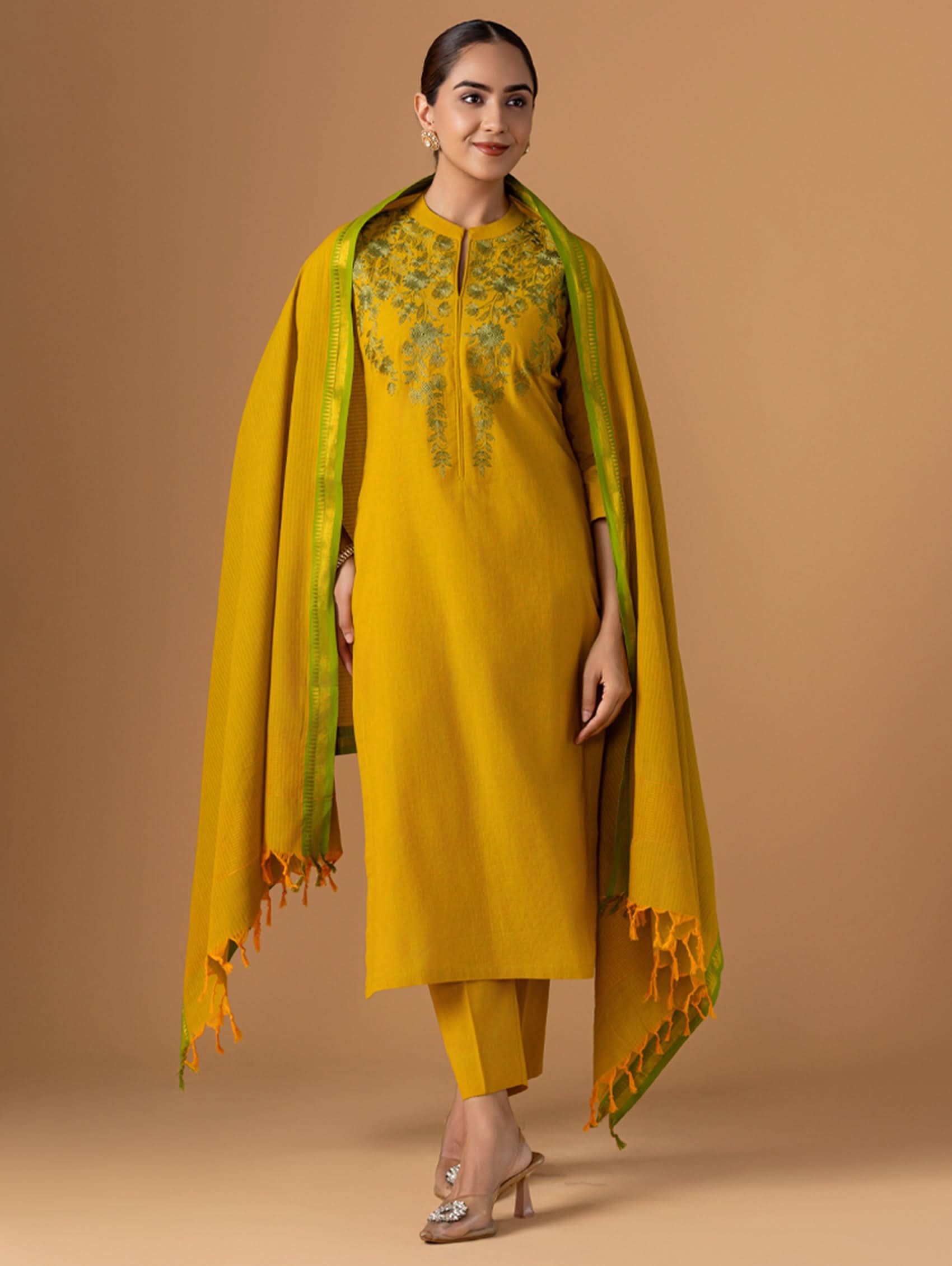 Woman wearing a yellow outfit with a green dupatta against a brown background
