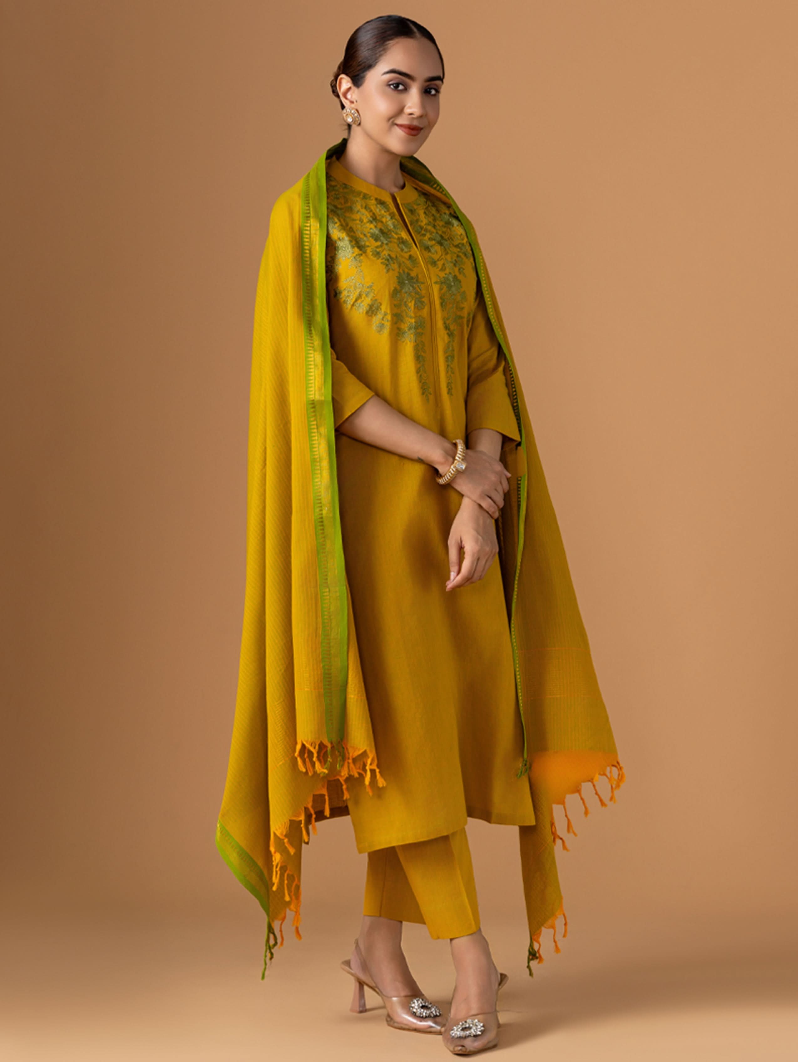 Woman wearing a mustard yellow outfit with a green and orange dupatta against a brown background