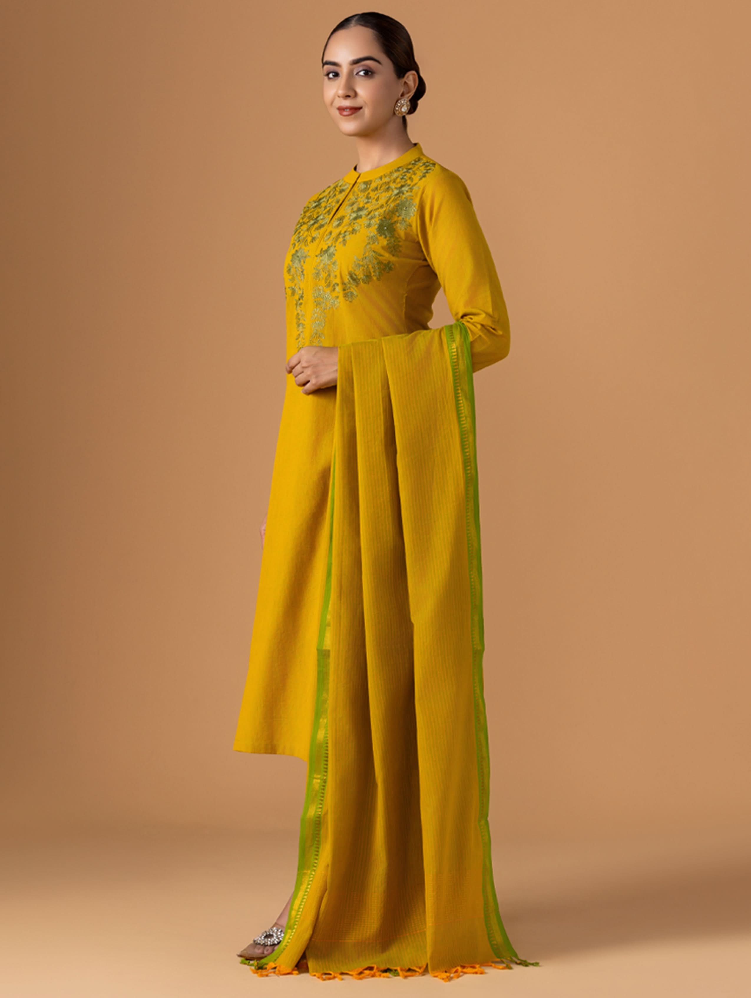 Woman wearing a yellow traditional outfit with a matching dupatta on a beige background