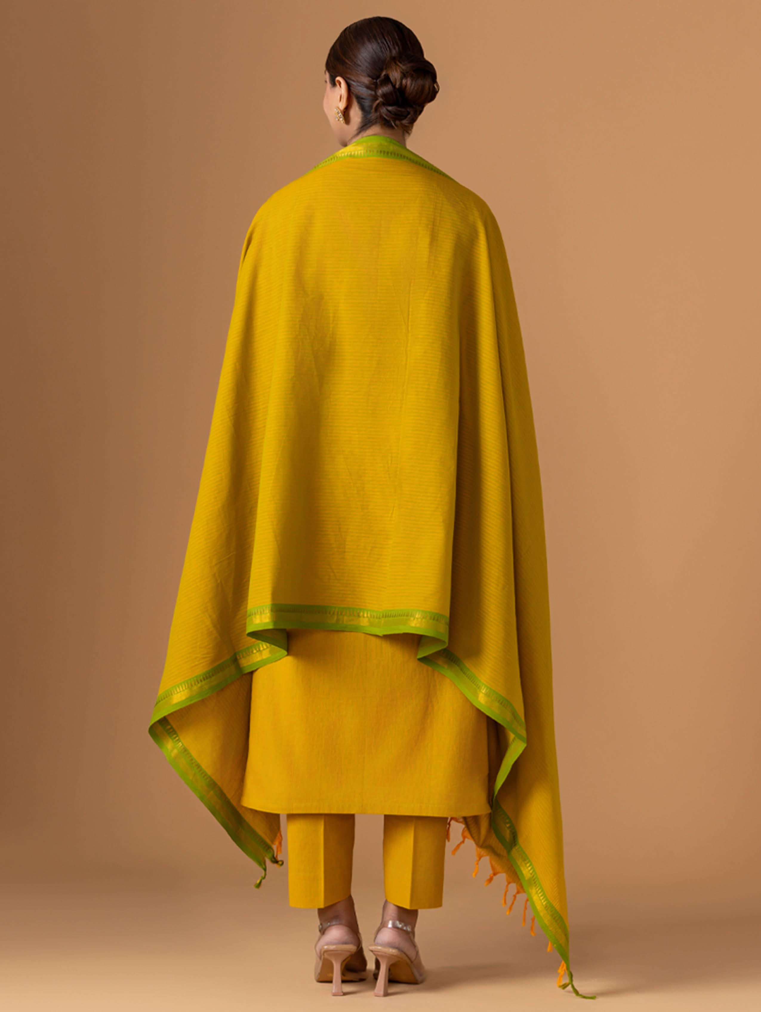 Person wearing a mustard yellow outfit with a green border against a beige background