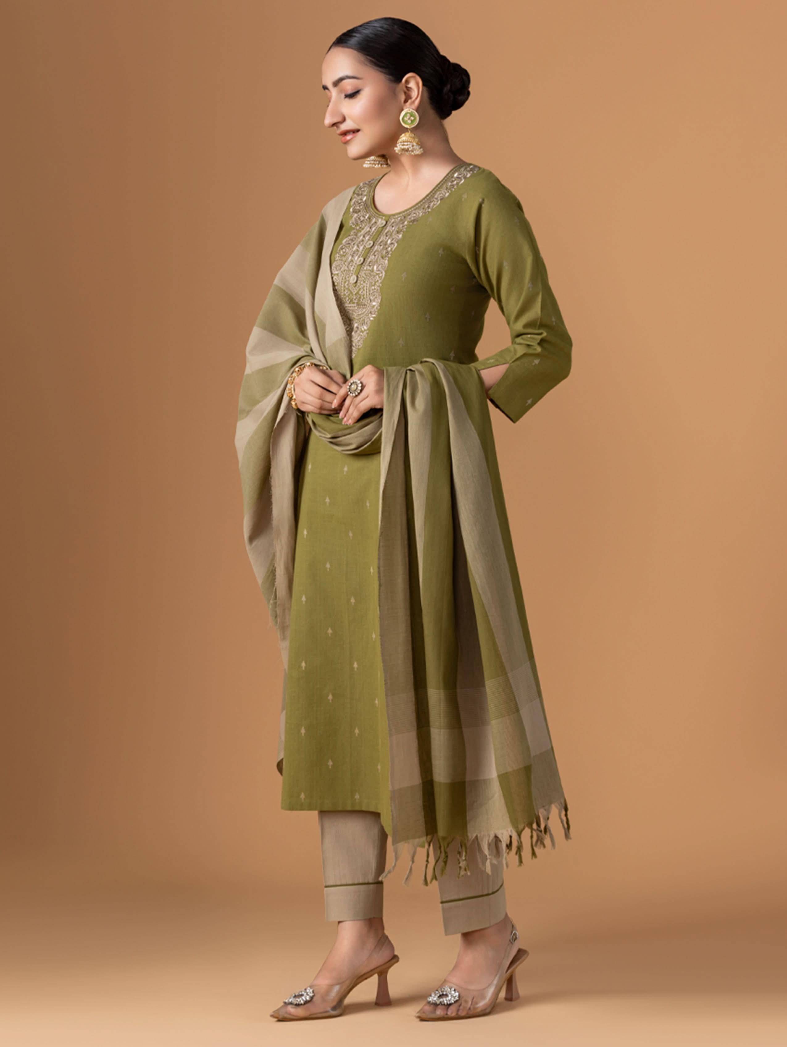 Woman wearing a green traditional outfit with a beige shawl on a brown background