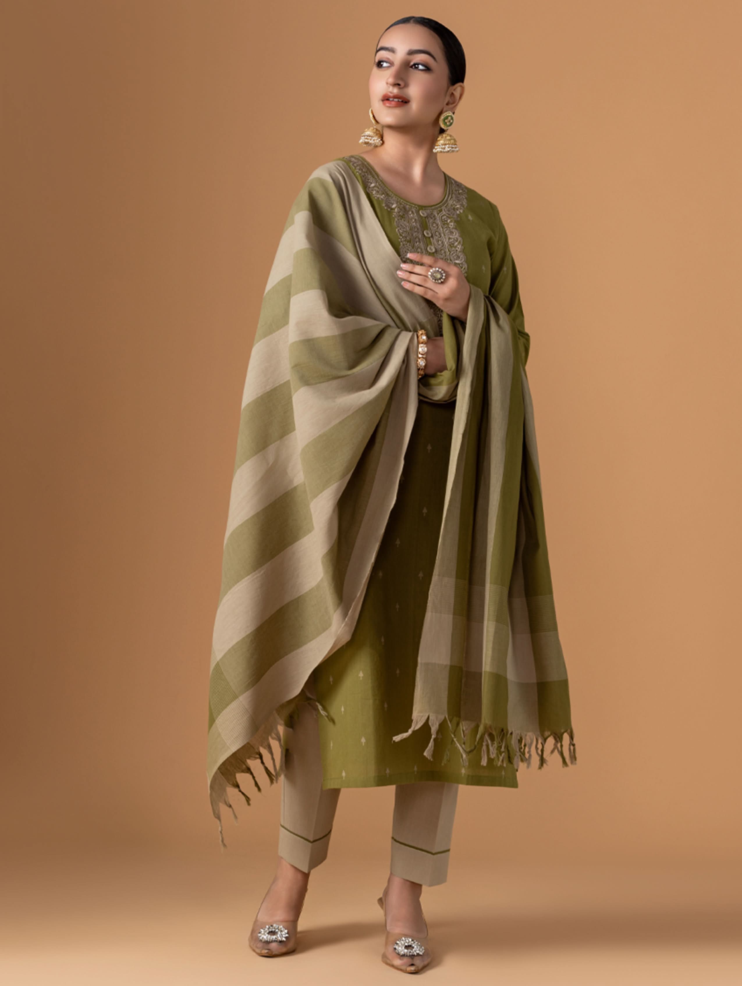 Woman wearing a green and beige traditional outfit with a matching shawl on a brown background