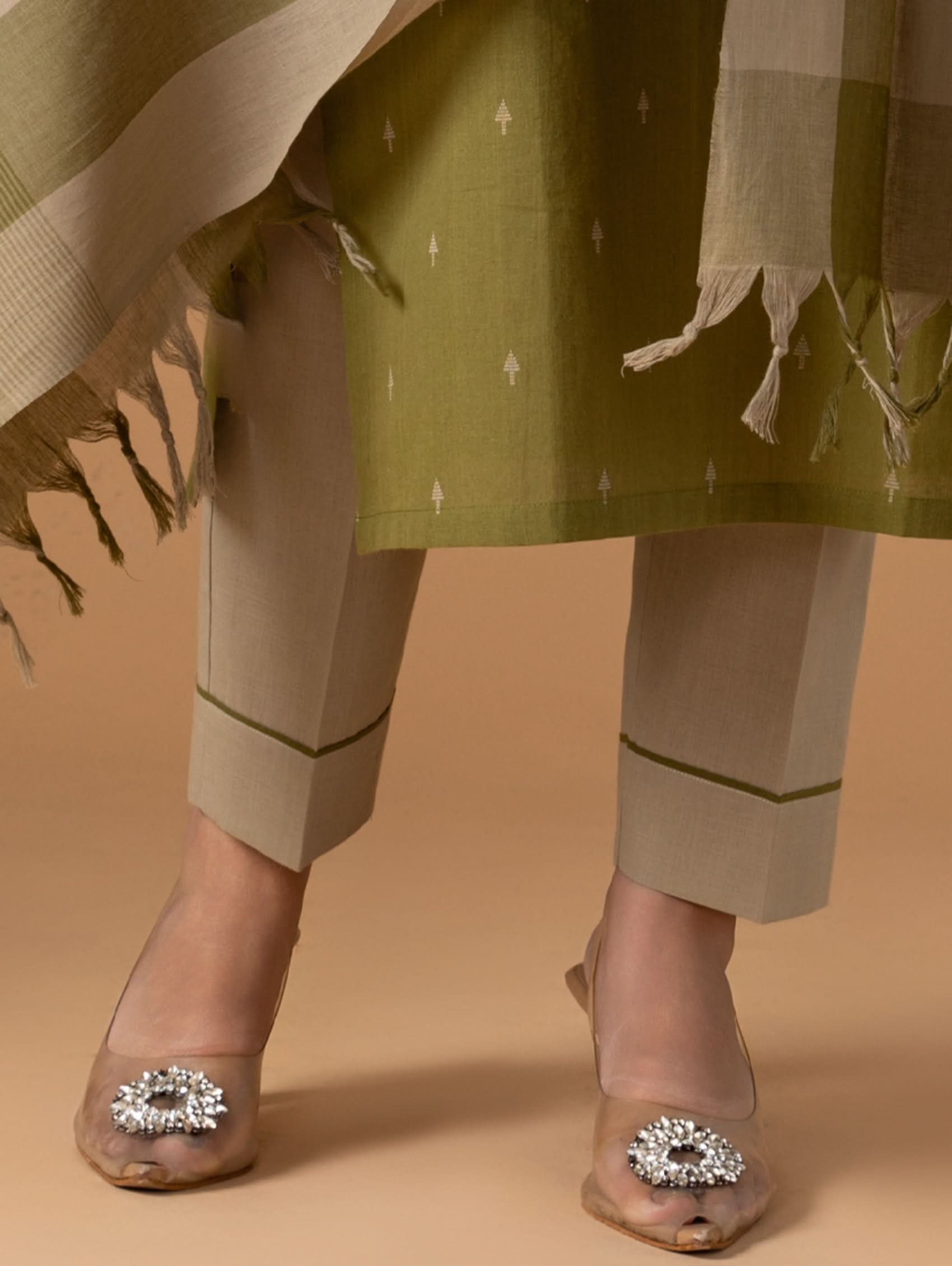 Person wearing a green outfit with beige accents and embellished sandals on a beige background