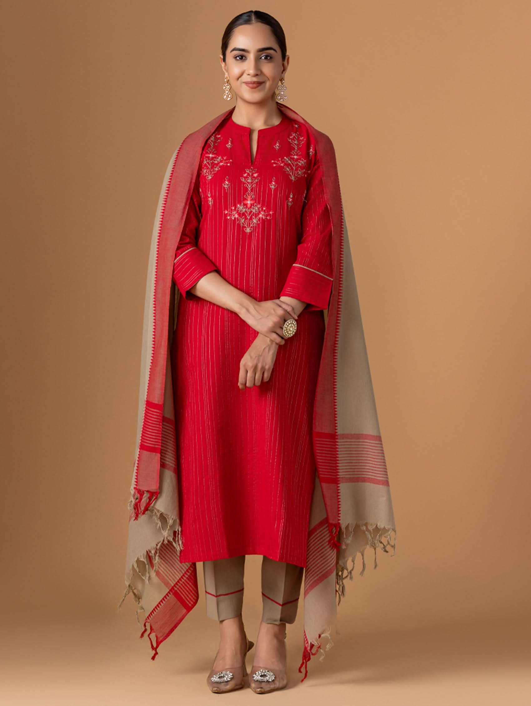 Woman wearing a red traditional outfit with a beige dupatta on a brown background