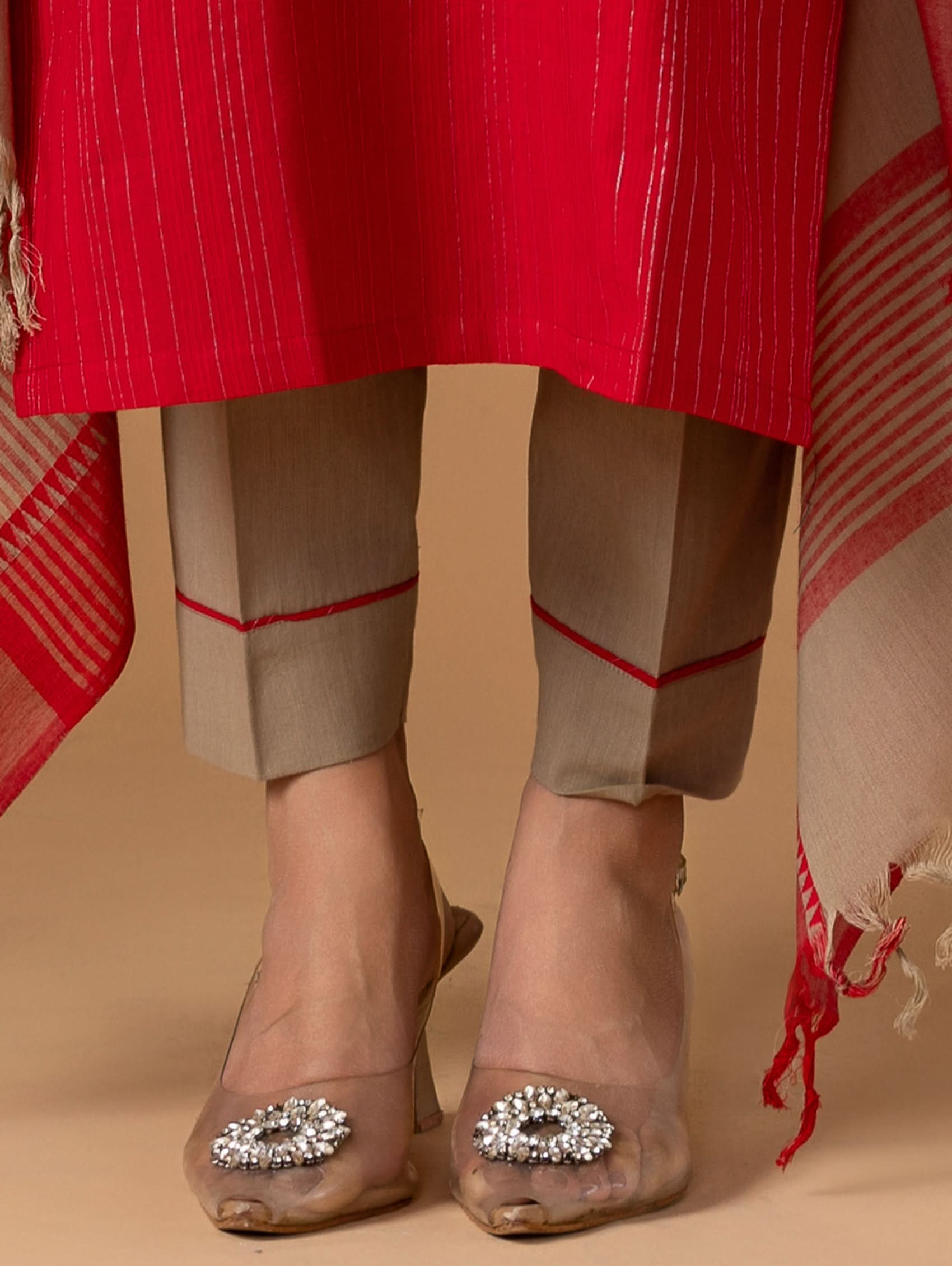 Person wearing a red coat, beige pants, and brown shoes with decorative embellishments on a beige background