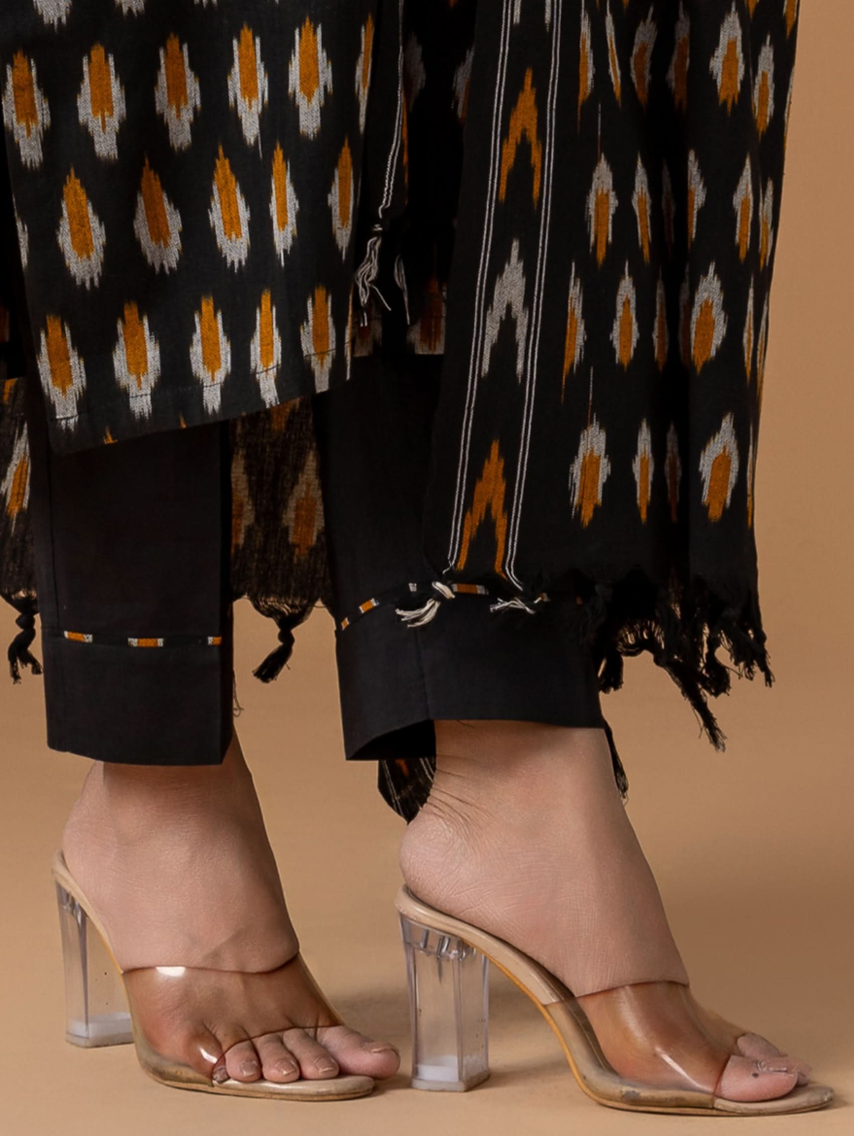Clear high-heeled sandals worn with a patterned outfit on a beige background