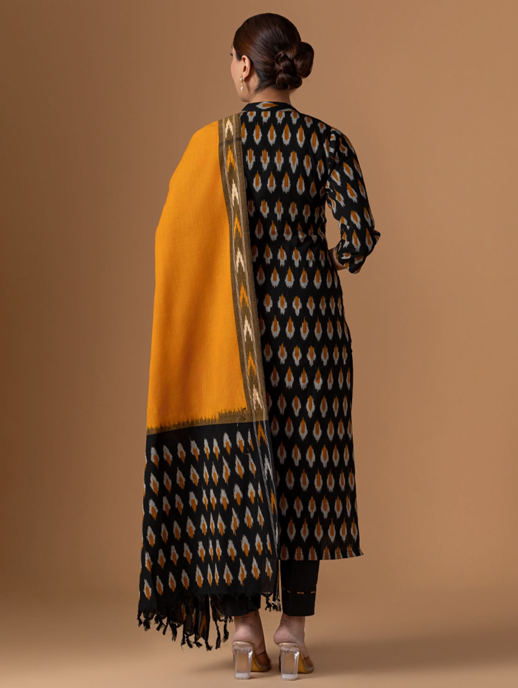 Woman wearing a black and gold patterned kurta with a mustard yellow dupatta on a brown background