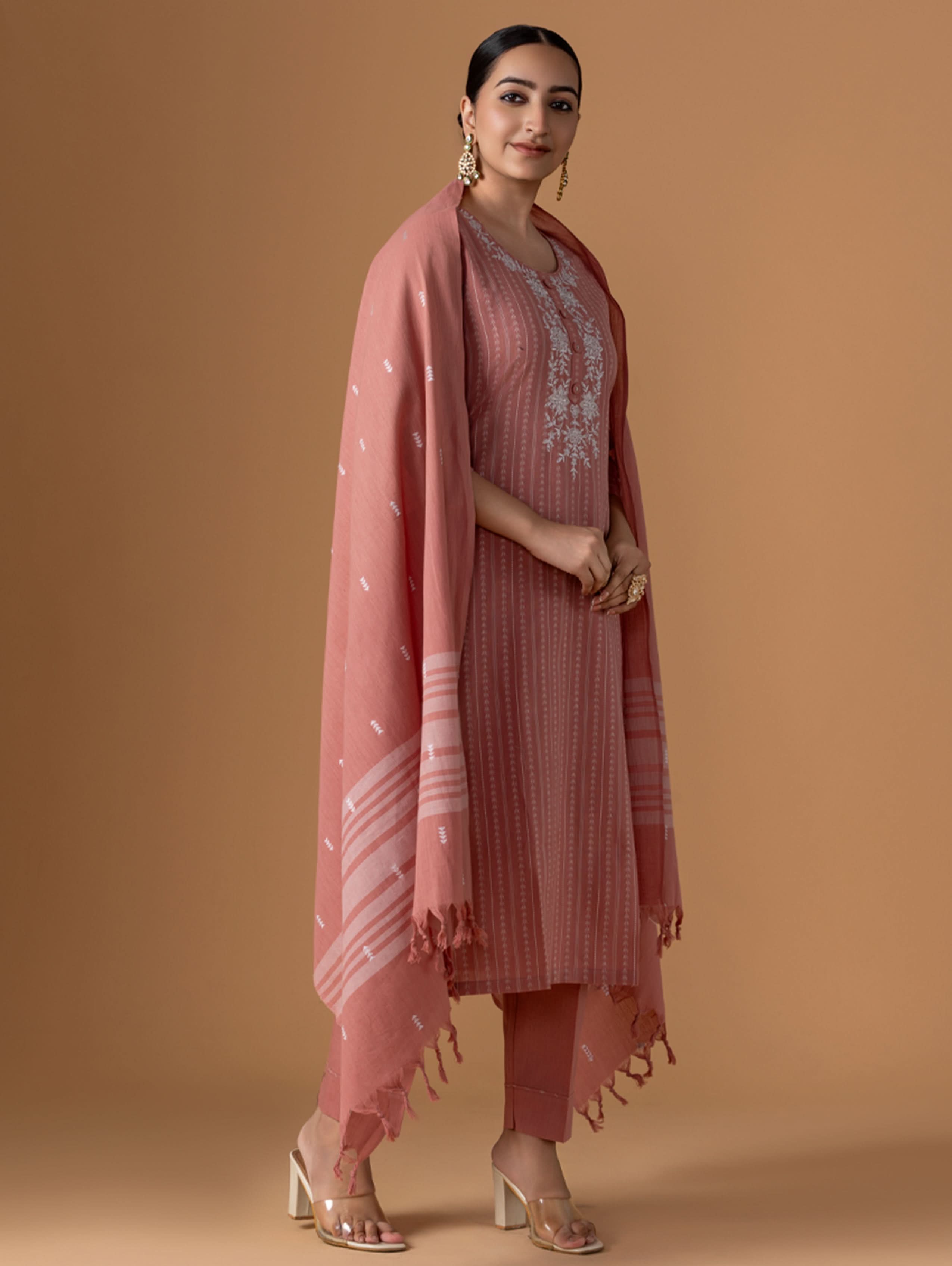 Woman wearing a pink traditional outfit with a matching dupatta against a brown background