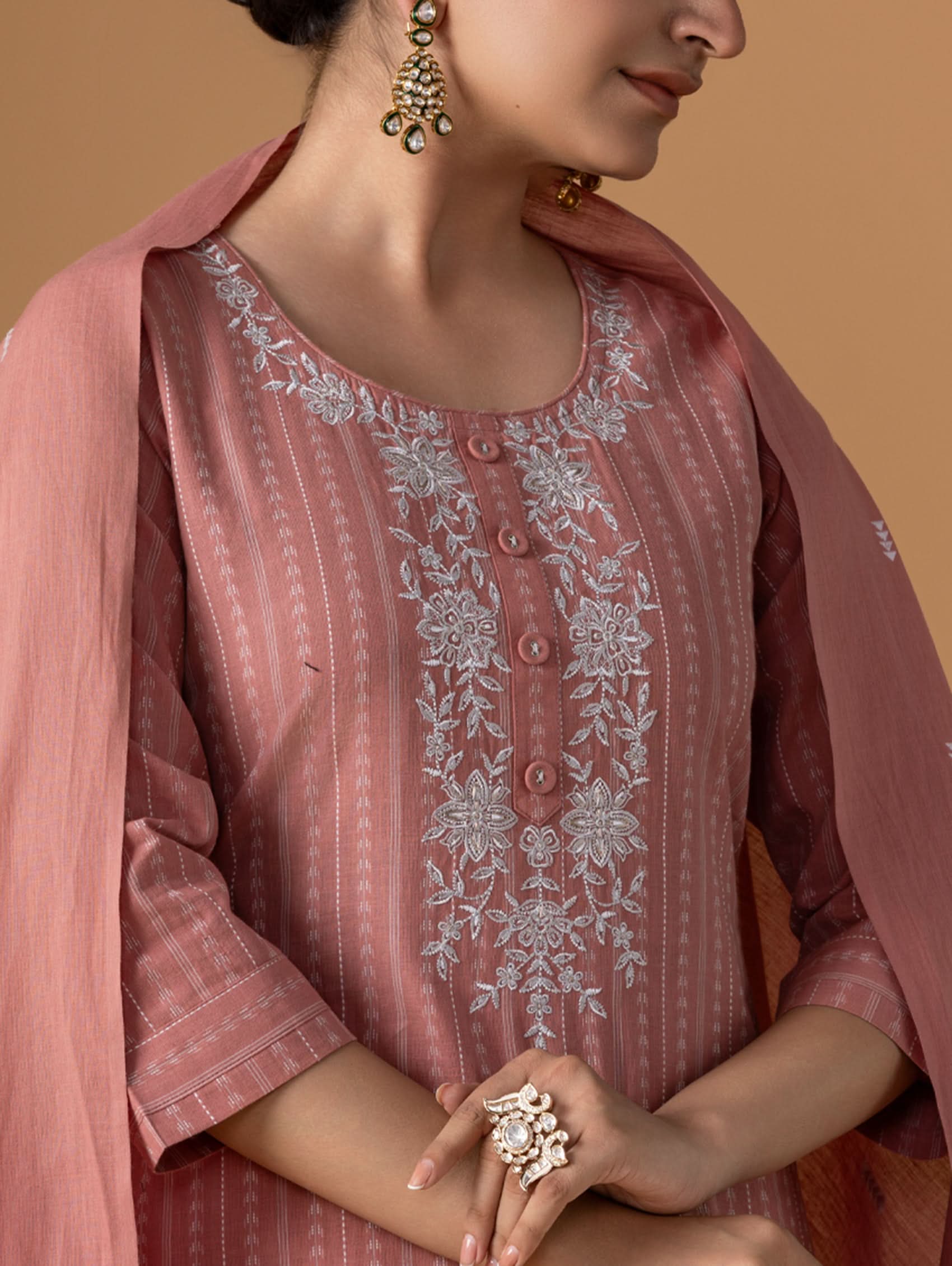 Woman wearing a pink embroidered traditional outfit with jewelry against a beige background
