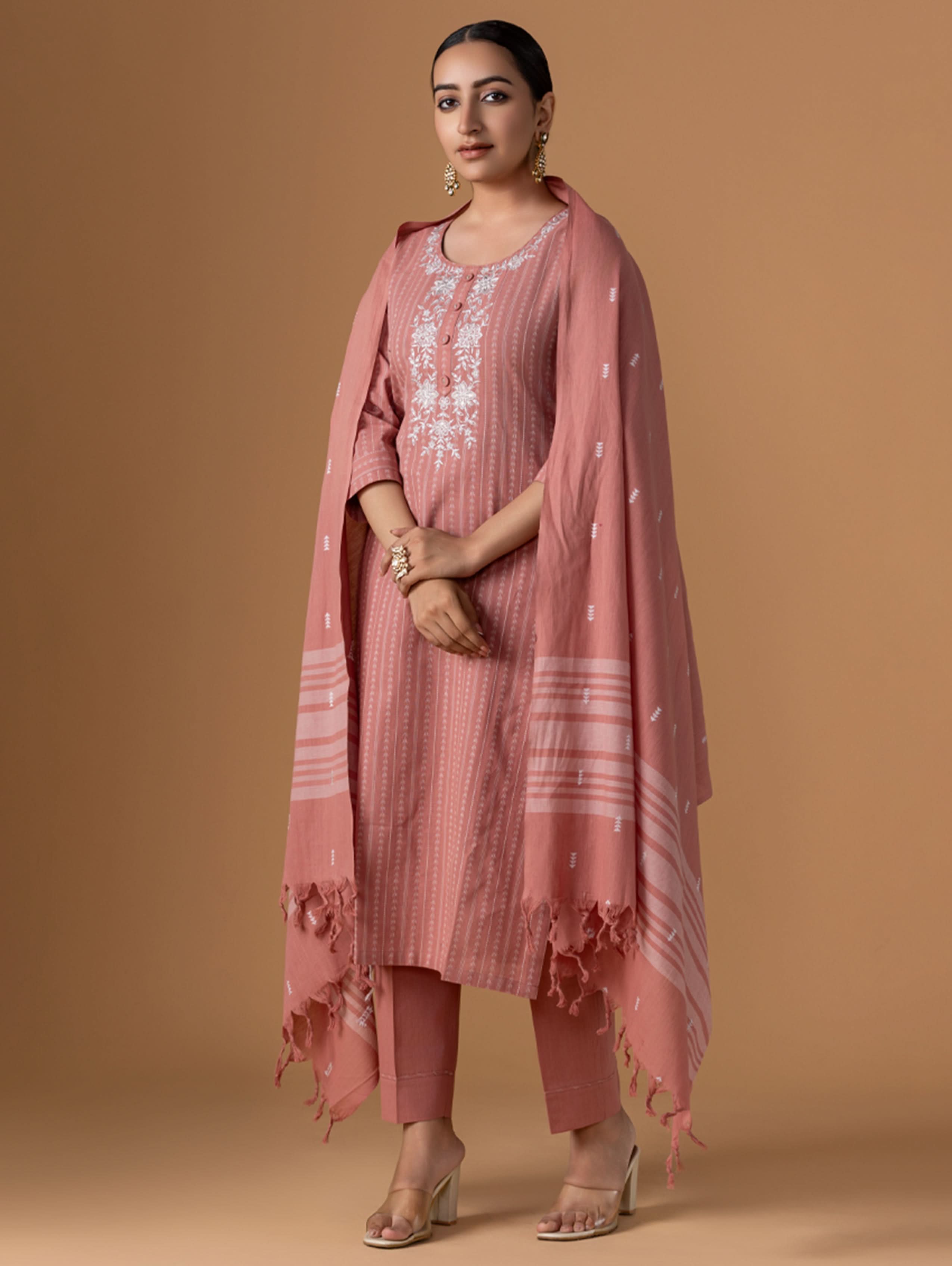 Woman wearing a pink traditional outfit with a matching dupatta on a beige background